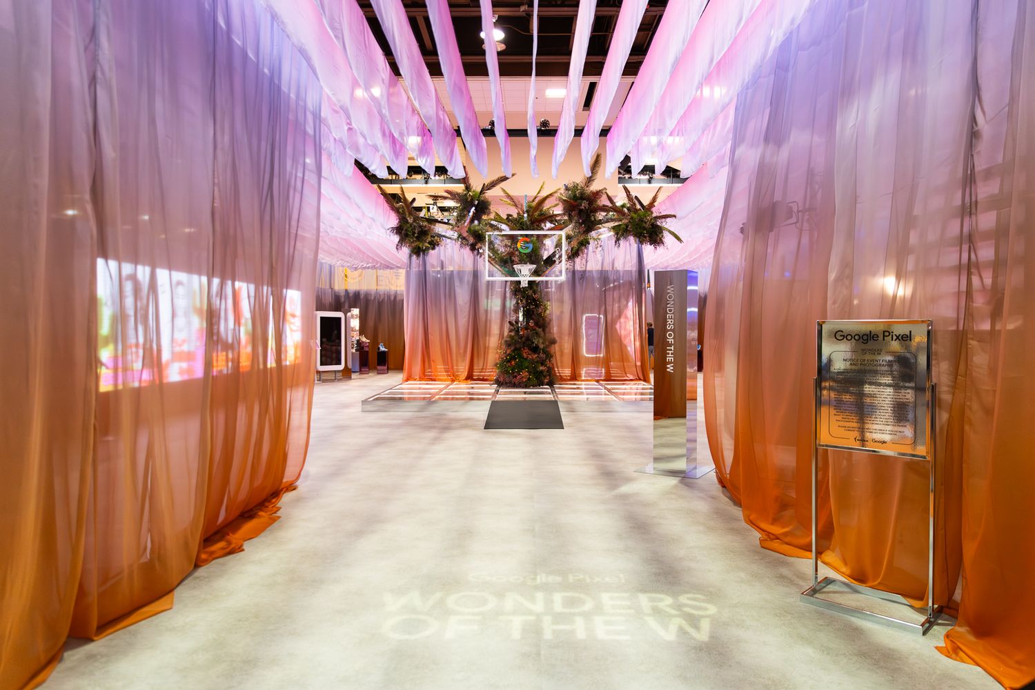 Elegant event entrance hallway with flowing orange drapes, dramatic floral installation, and glowing floor projection.