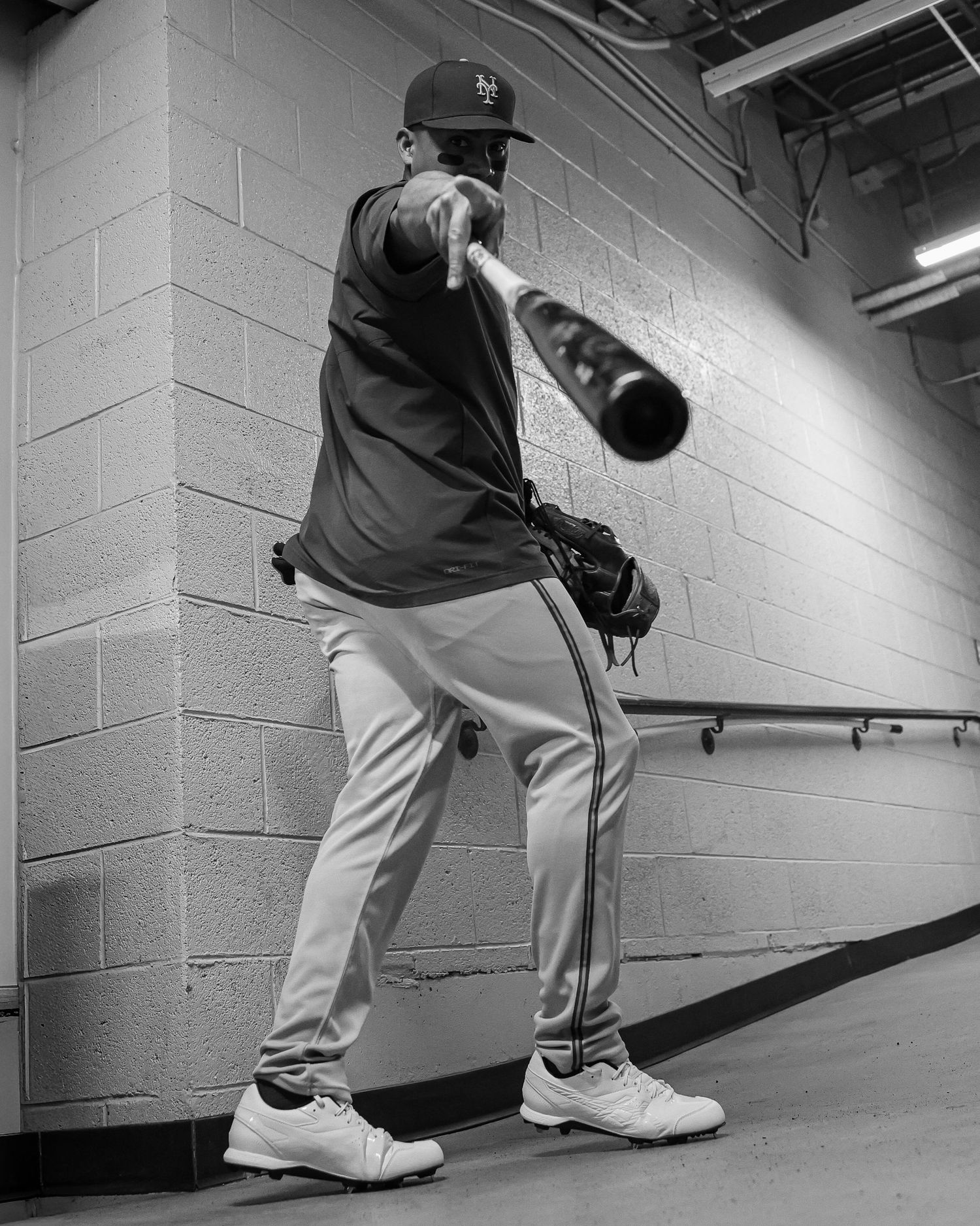 A New York Mets player practices his batting swing in the stadium tunnel in black and white.