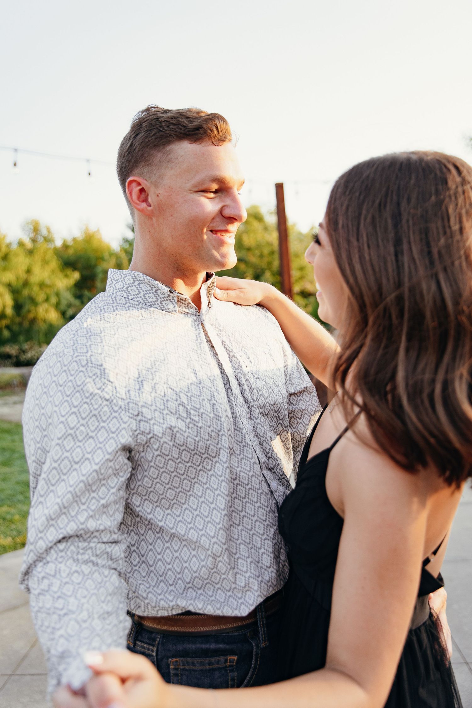 A smiling couple dances outdoors at sunset, with the woman in a black dress placing her hand on the man's chest.