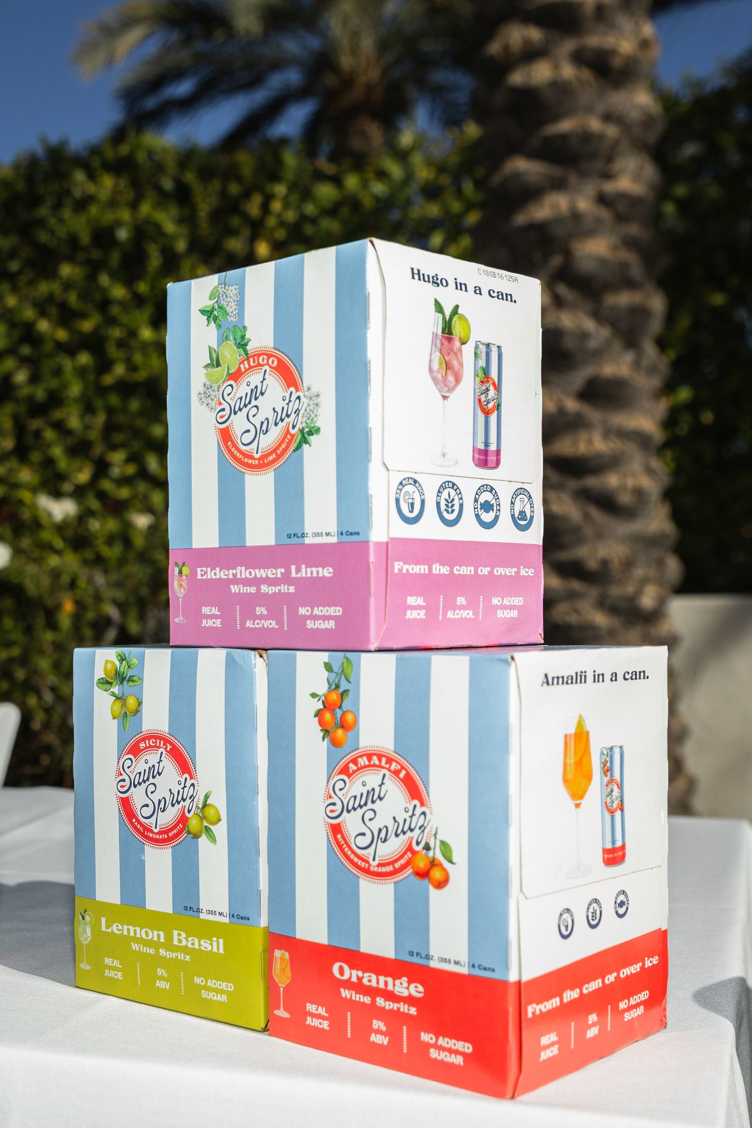 Stacked boxes of Saint Spritz canned wine spritzers in flavors including Elderflower Lime and Lemon Basil outdoors.