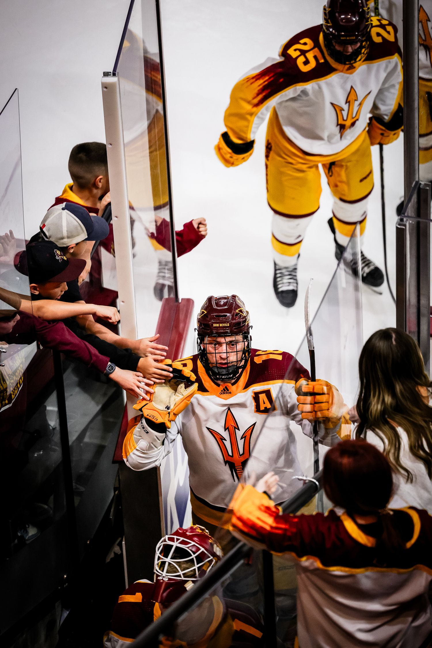 ASU hockey players in white uniforms high-five fans while exiting the ice after a game.