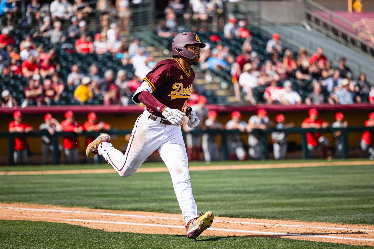 Arizona State Sun Devils baseball player sprints the bases in maroon and gold uniform during a college game.