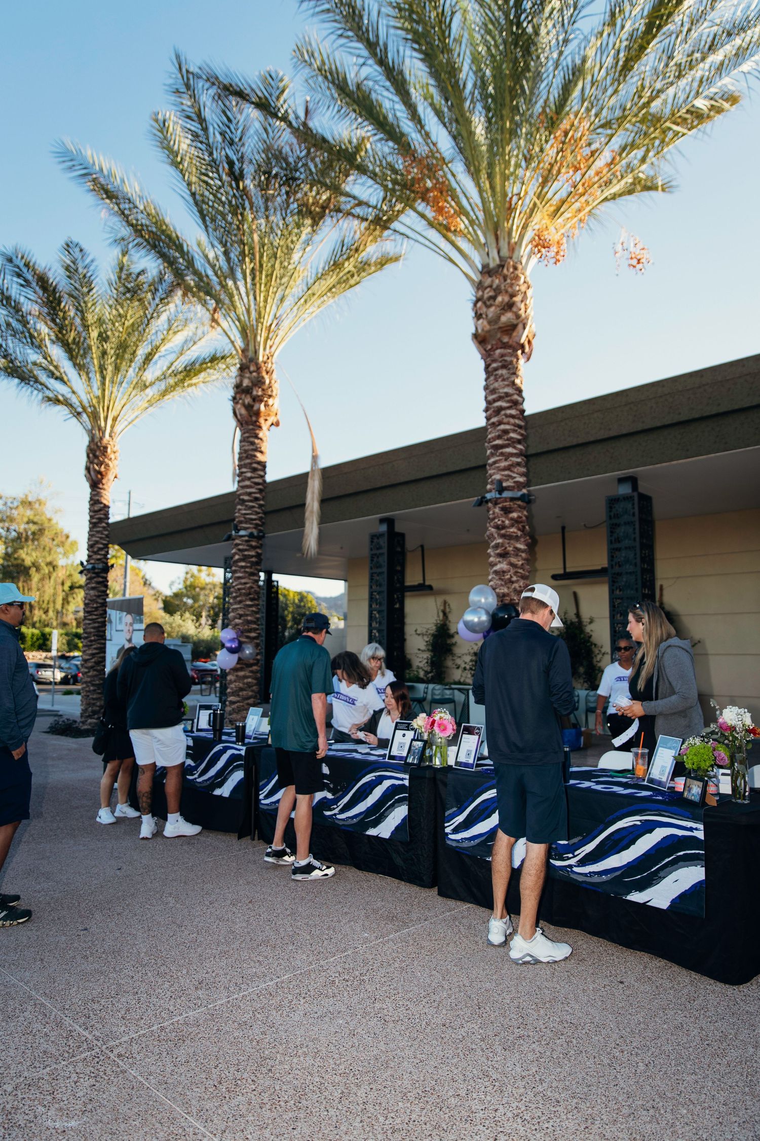 Guests browse silent auction tables under palm trees at an outdoor golf charity event at dusk.