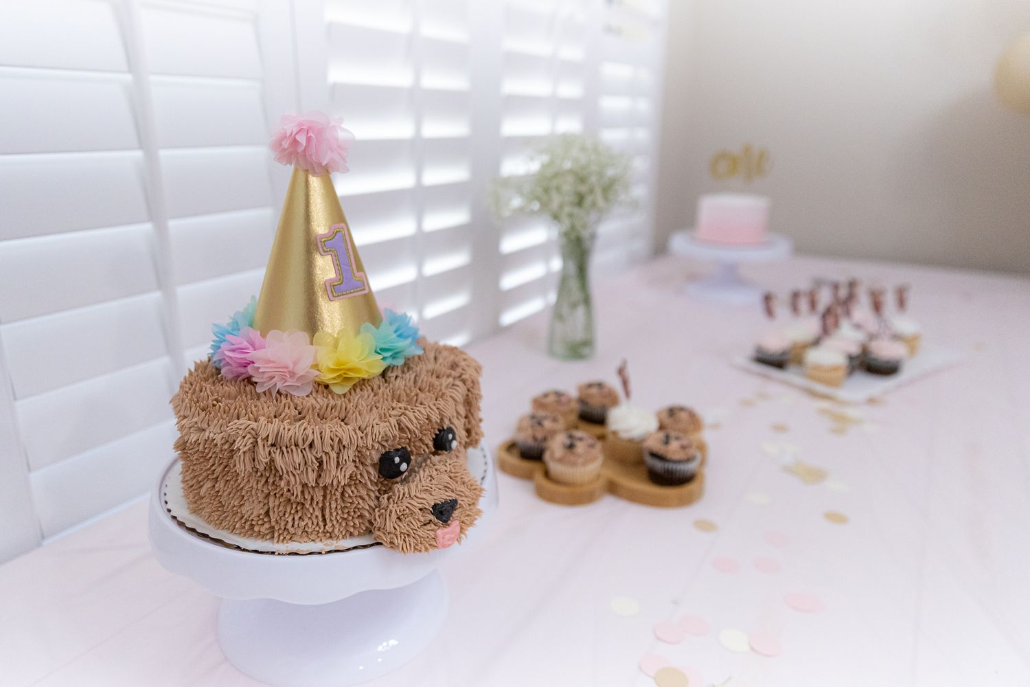 Adorable teddy bear birthday cake with a gold party hat on a white cake stand.