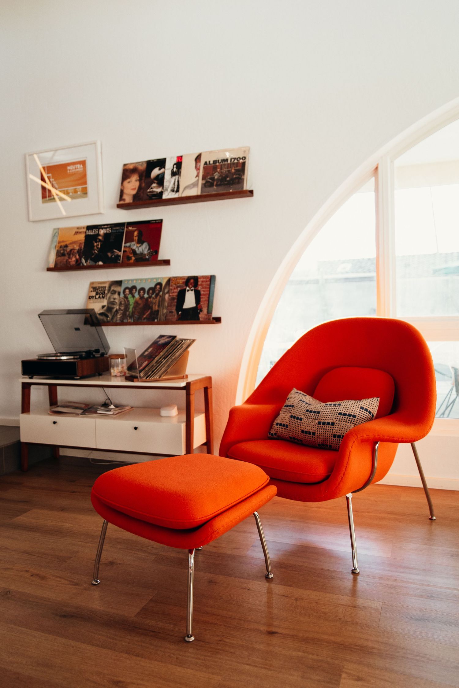 Mid-century modern orange Womb chair with ottoman beside vinyl record shelves.