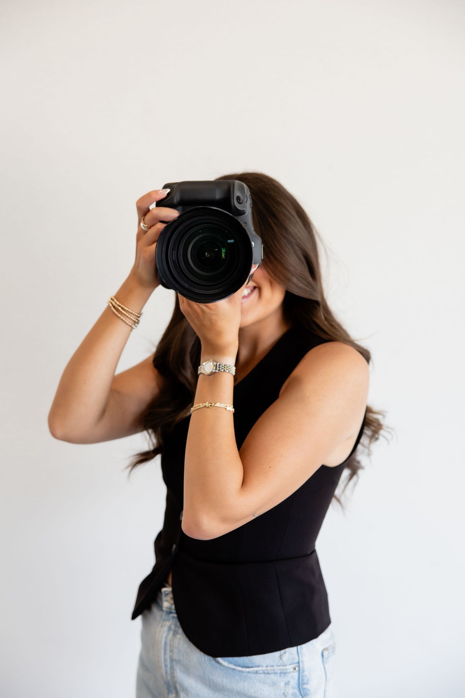 Female photographer holding a professional DSLR camera up to her face against a white background.