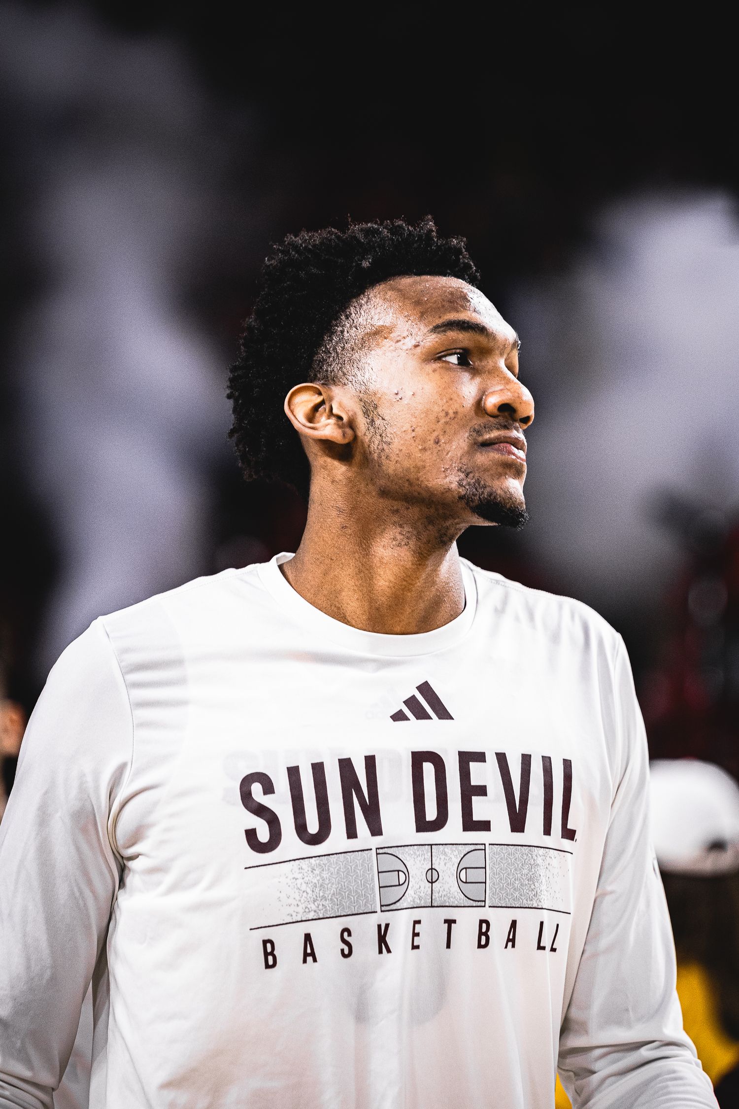 Arizona State Sun Devil Basketball player in white adidas warmup shirt gazes intently before a home game.