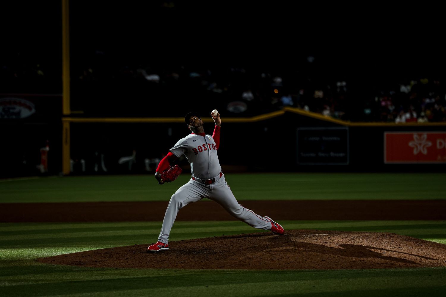 Baseball pitcher in red and white uniform winds up for a pitch under stadium lights at night.