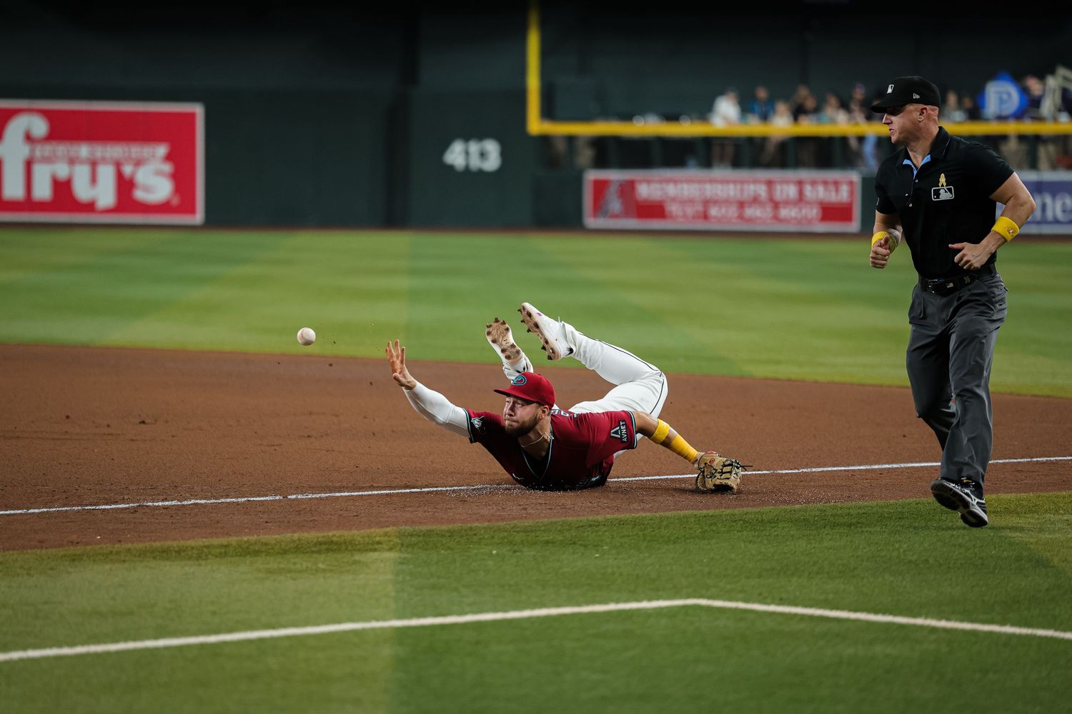 Baseball player dives on field while umpire watches during night game at stadium.