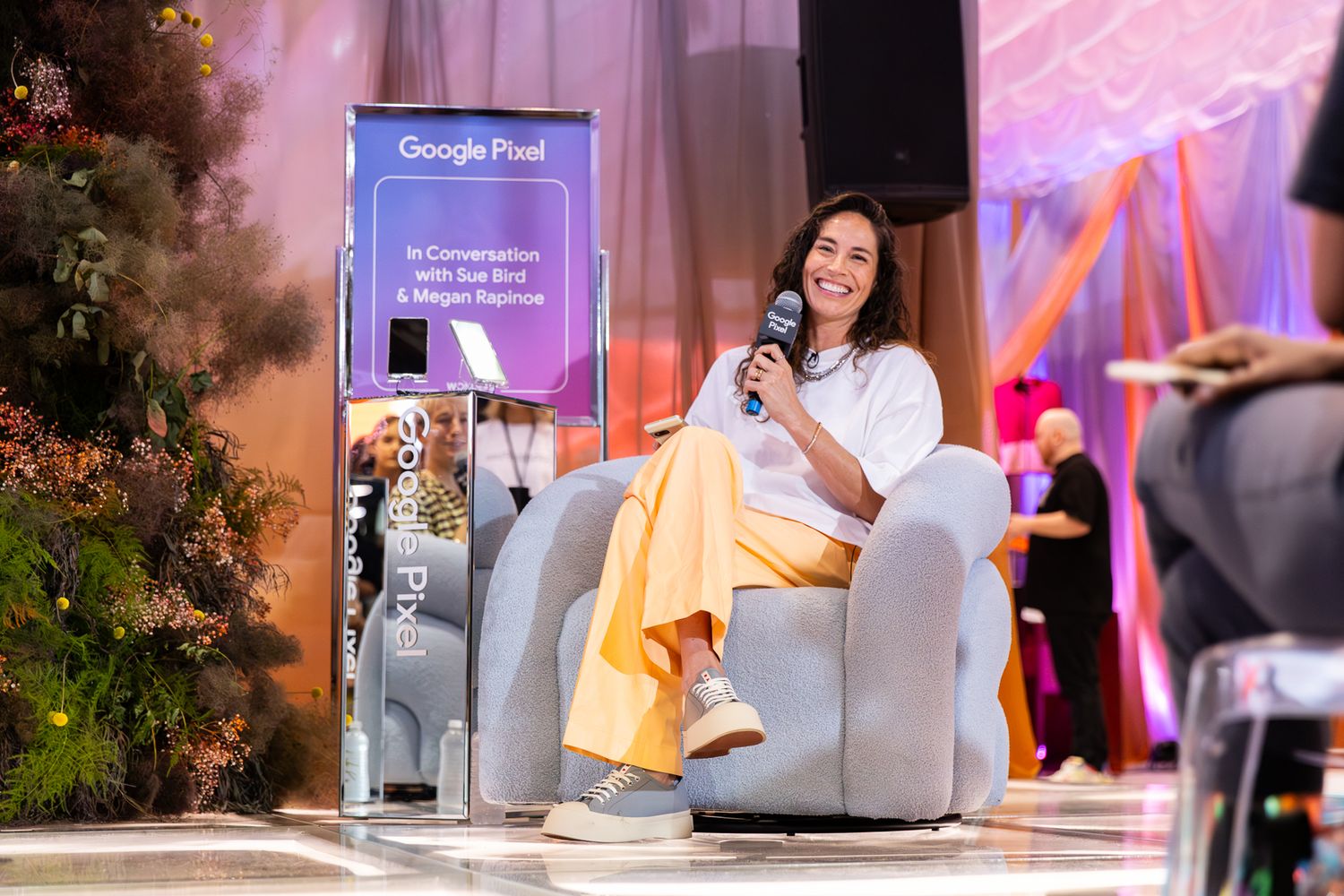 Woman in white outfit sits in a modern chair on stage at a Google Pixel sponsored panel event.