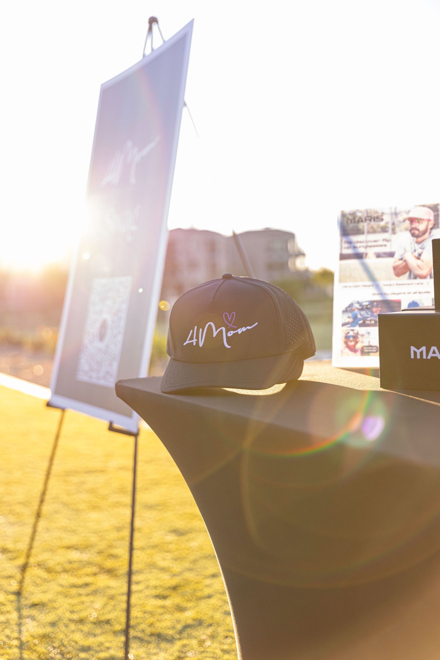 Signed snapback hat displayed on table at outdoor charity golf event at sunset.