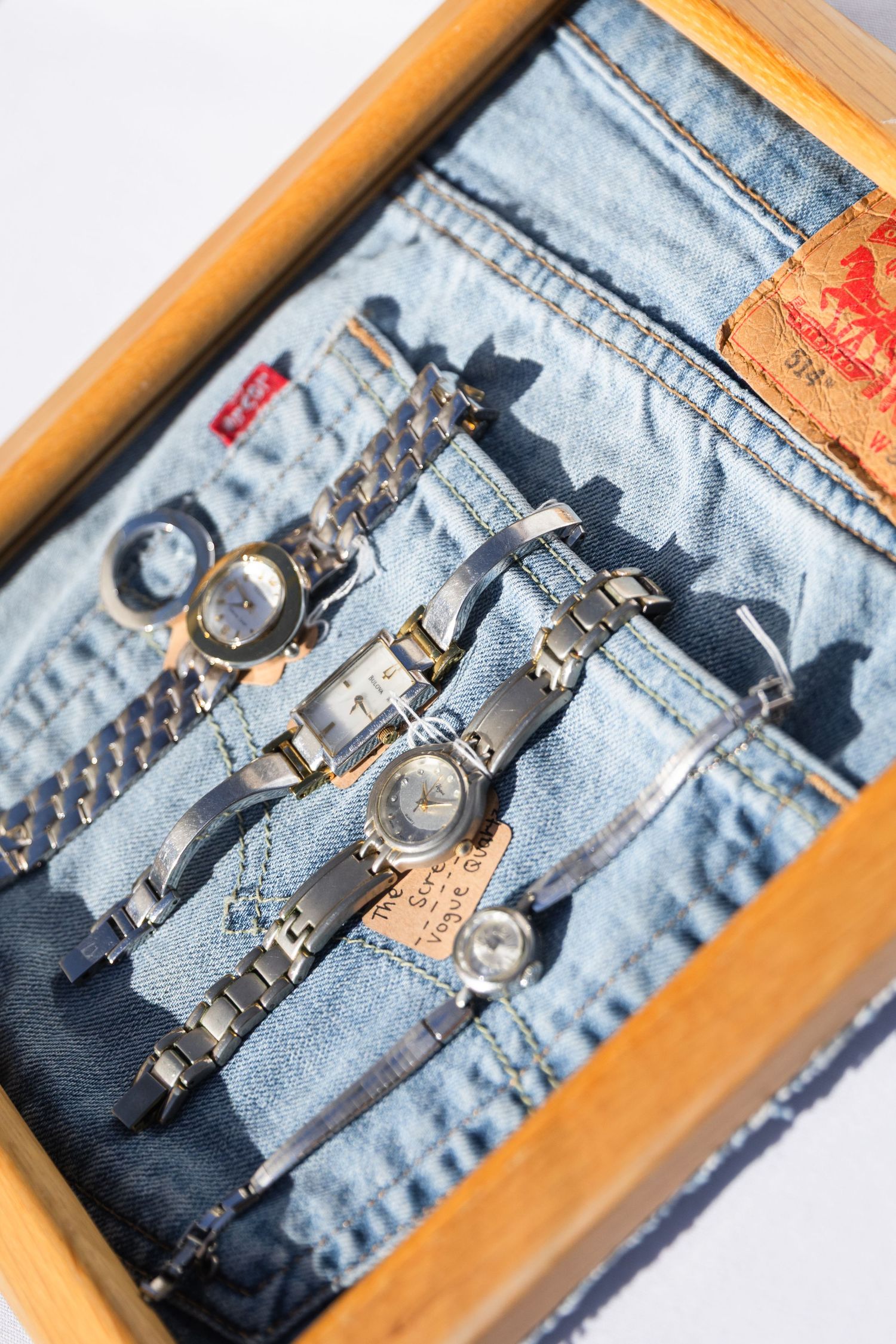 Collection of silver watches displayed on Levi's denim jeans in wooden tray.