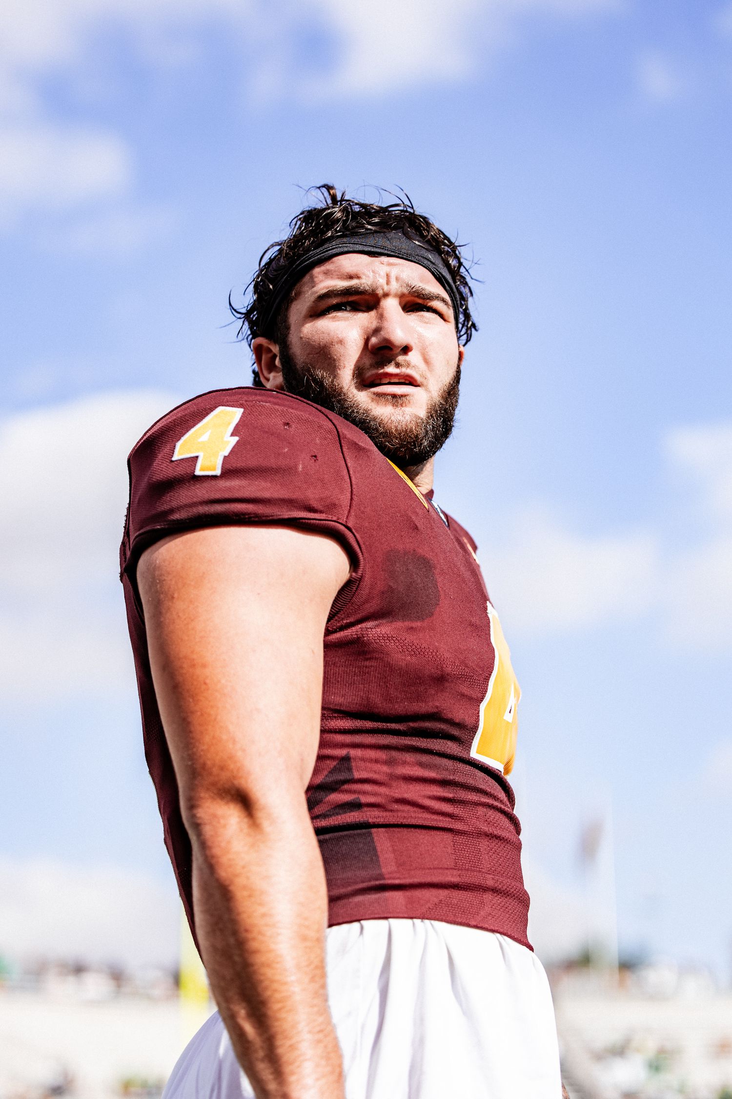 ASU Sun Devils football player number 4 in maroon jersey gazes forward under a blue sky.