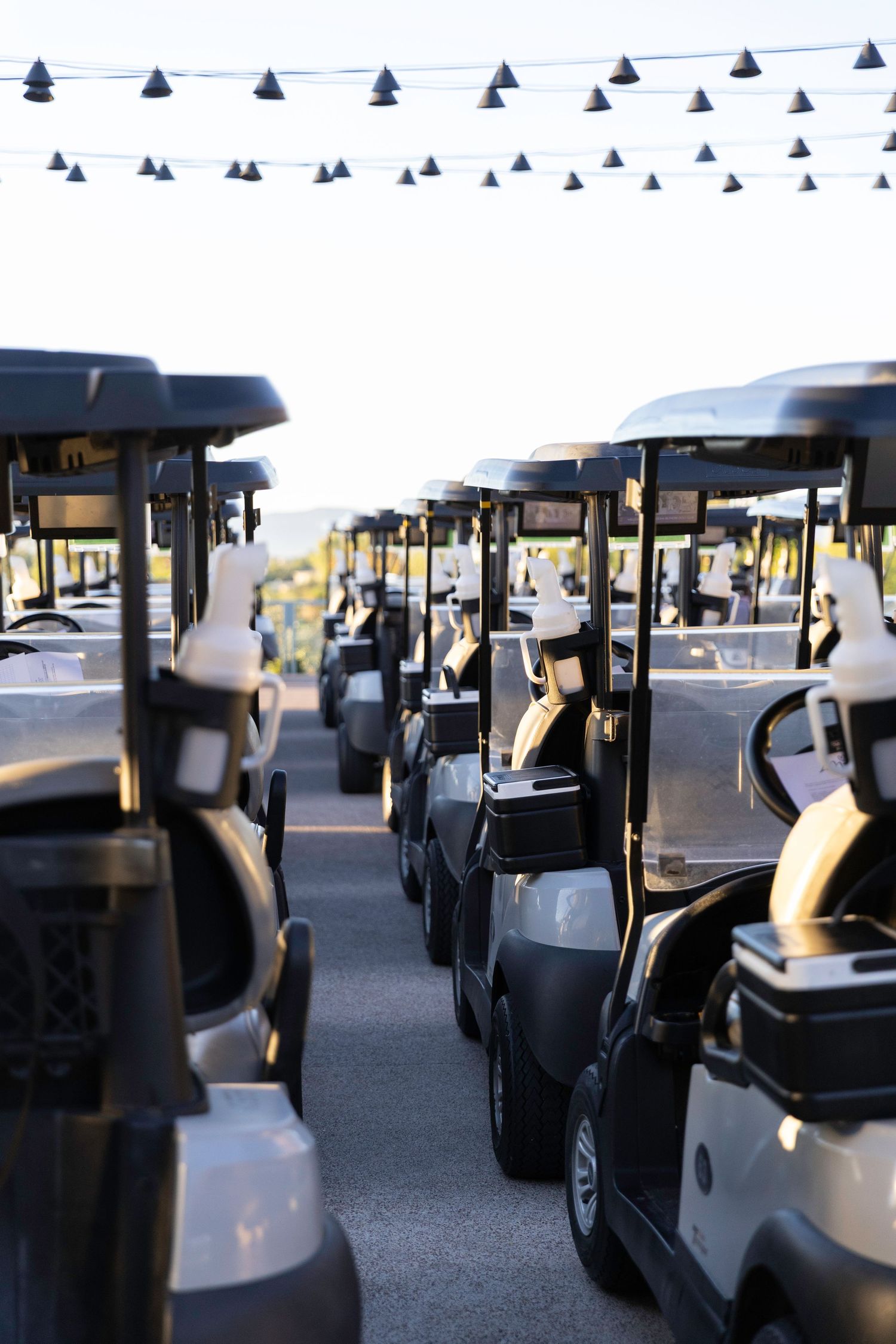 Rows of golf carts lined up at a sunny golf course event with string flag decorations overhead.
