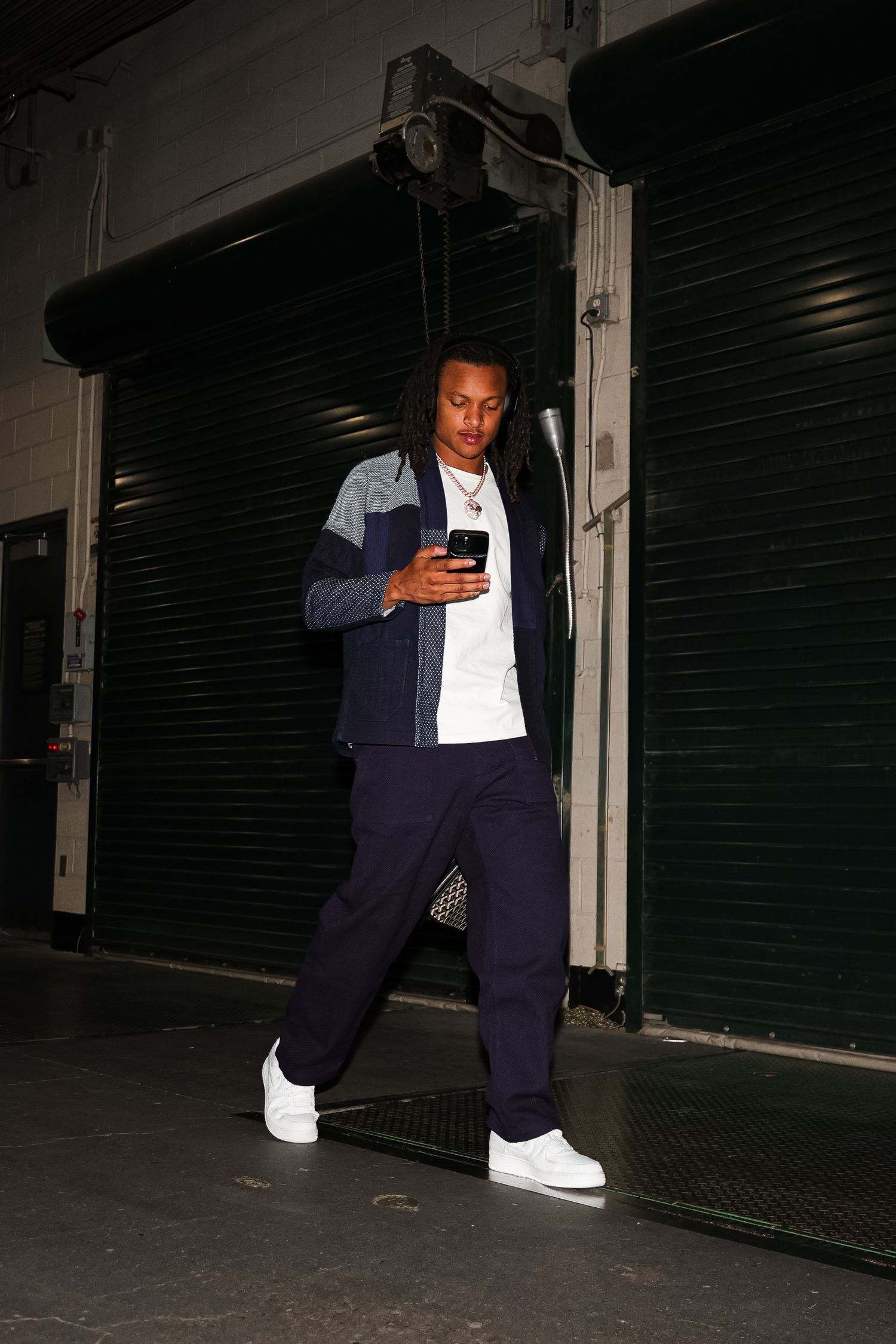 A young man with dreadlocks checks his phone while walking through a stadium garage entrance.