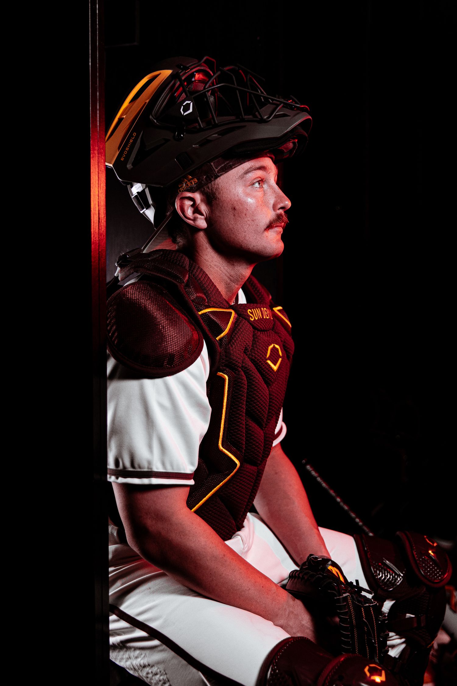 Arizona State baseball catcher sits in full maroon catching gear and white Devils uniform.