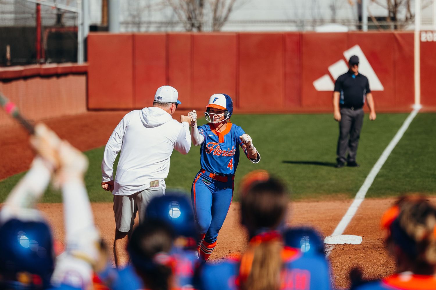 Boise State softball player receives high-five from coach while rounding bases in blue uniform.