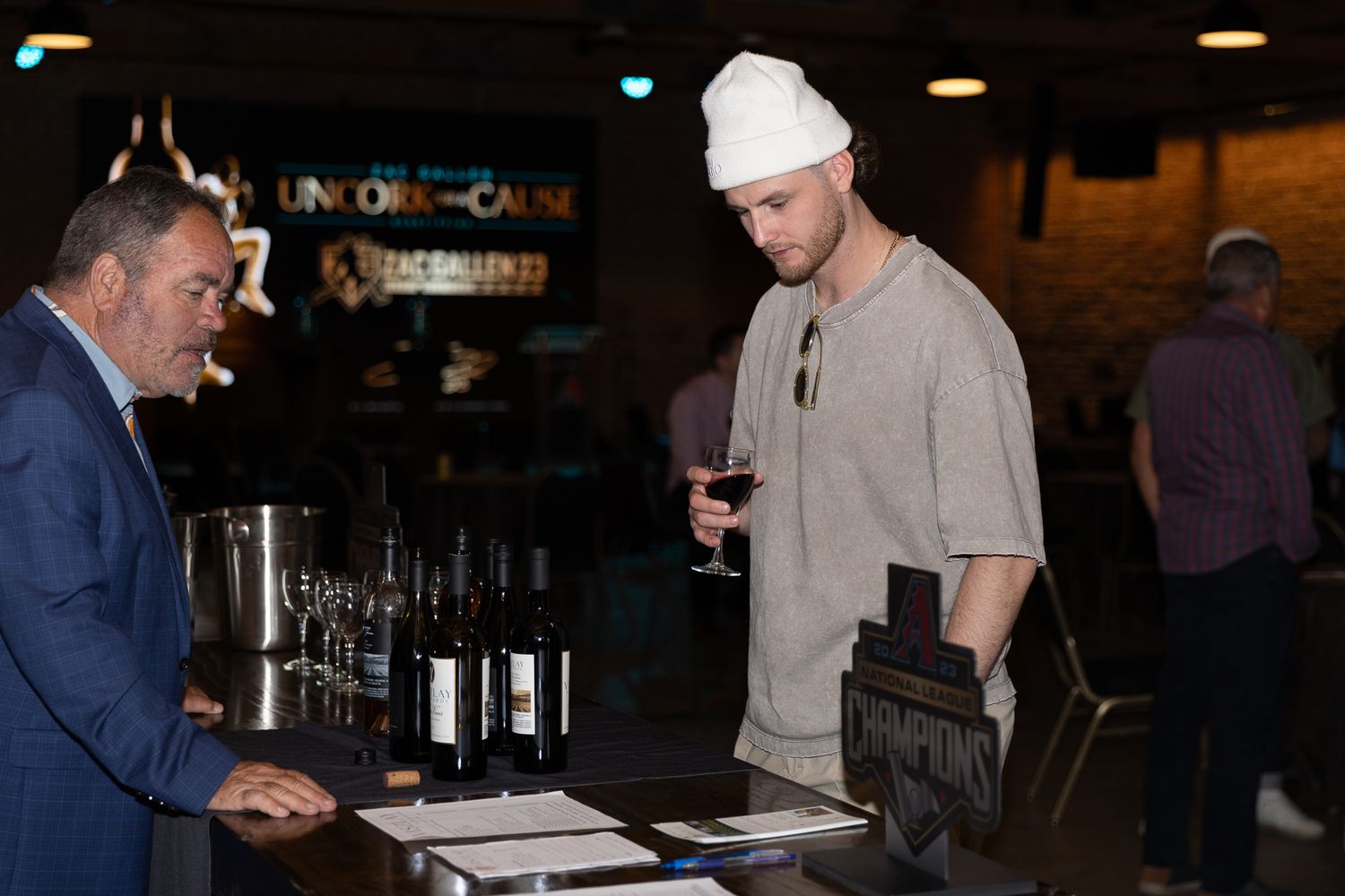 Two men conversing at wine bar during Uncork for a Cause fundraising event with bottles on counter.