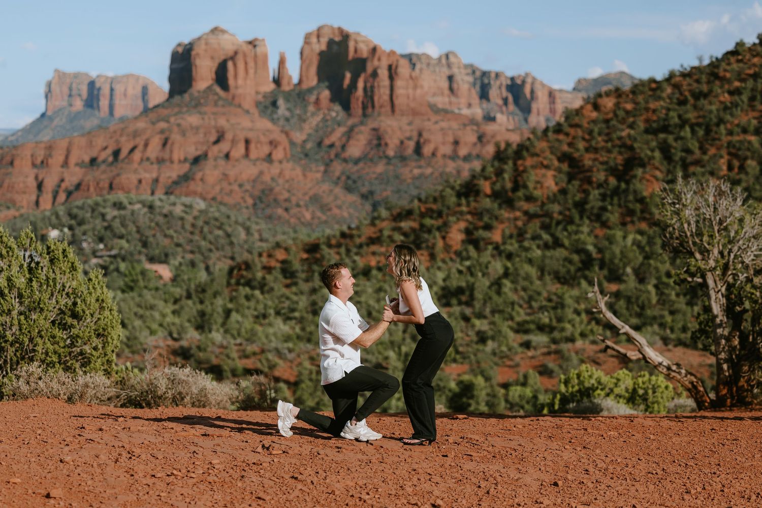 Couple's romantic marriage proposal on red rock terrain with stunning Sedona, Arizona red rock formations in the background.