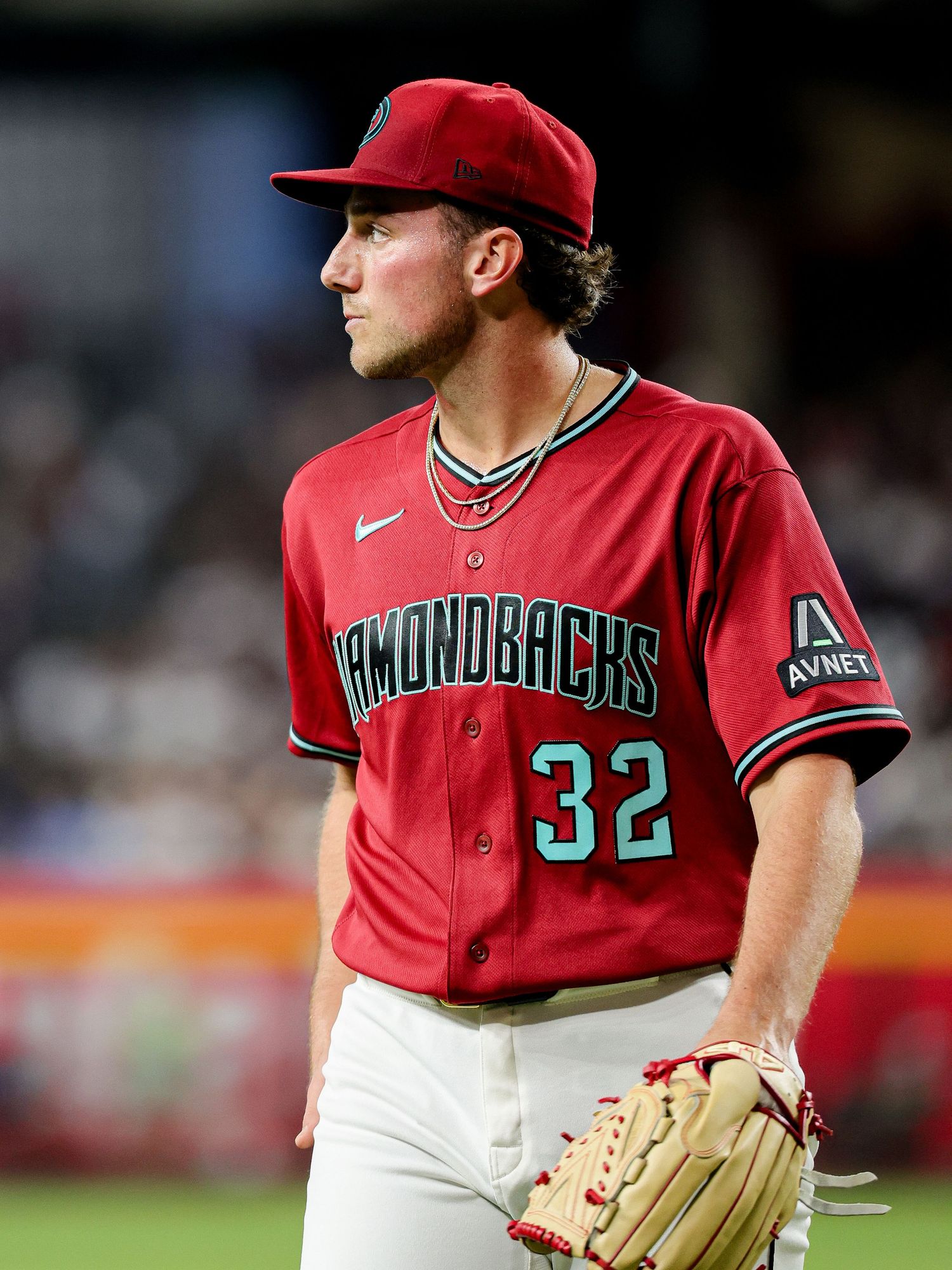 Arizona Diamondbacks pitcher #32 stands on the mound wearing a red and teal jersey during a night game.
