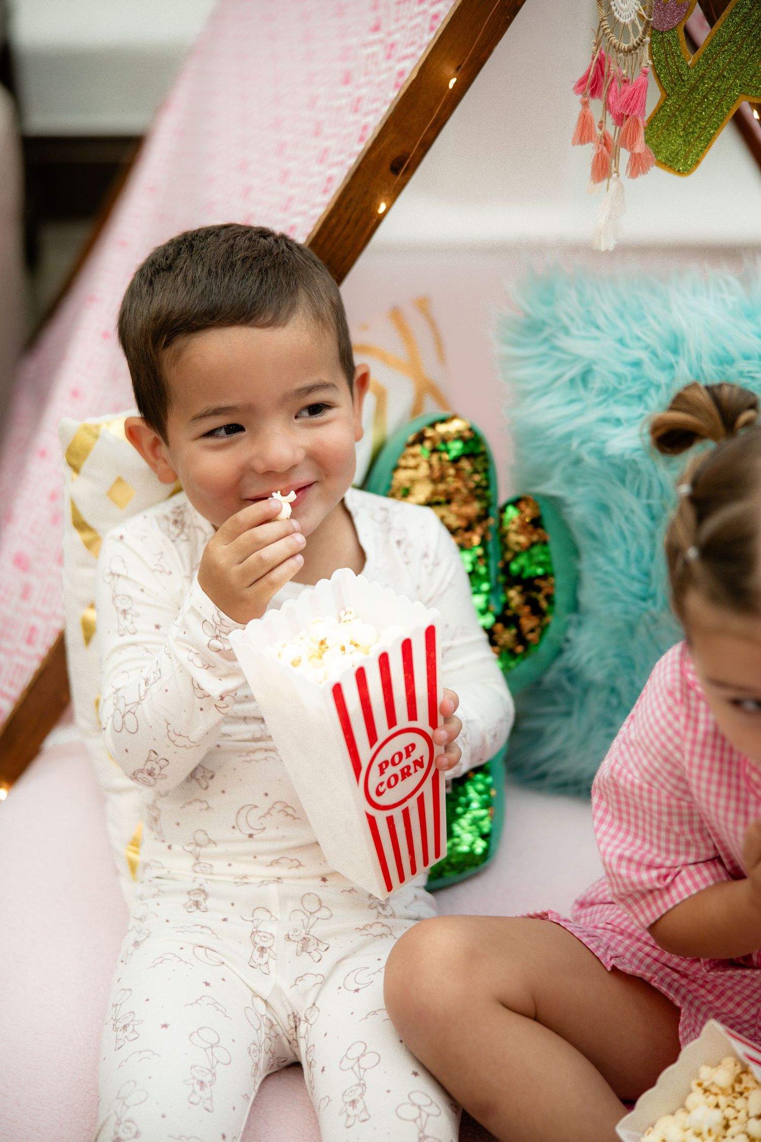 Happy young boy eating popcorn inside a decorated teepee at a kids party.