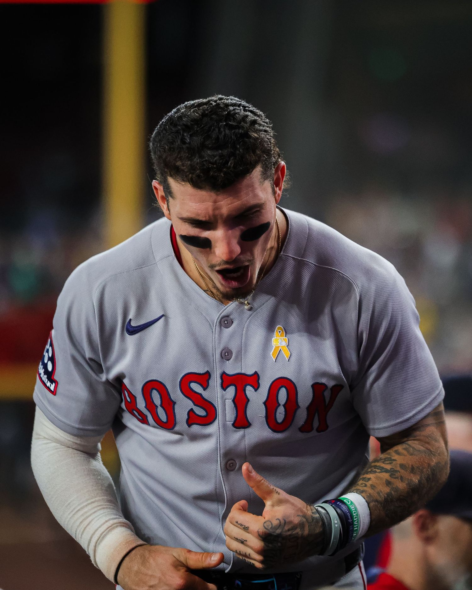 A Boston Red Sox player in gray away uniform walks in the dugout during a night game.