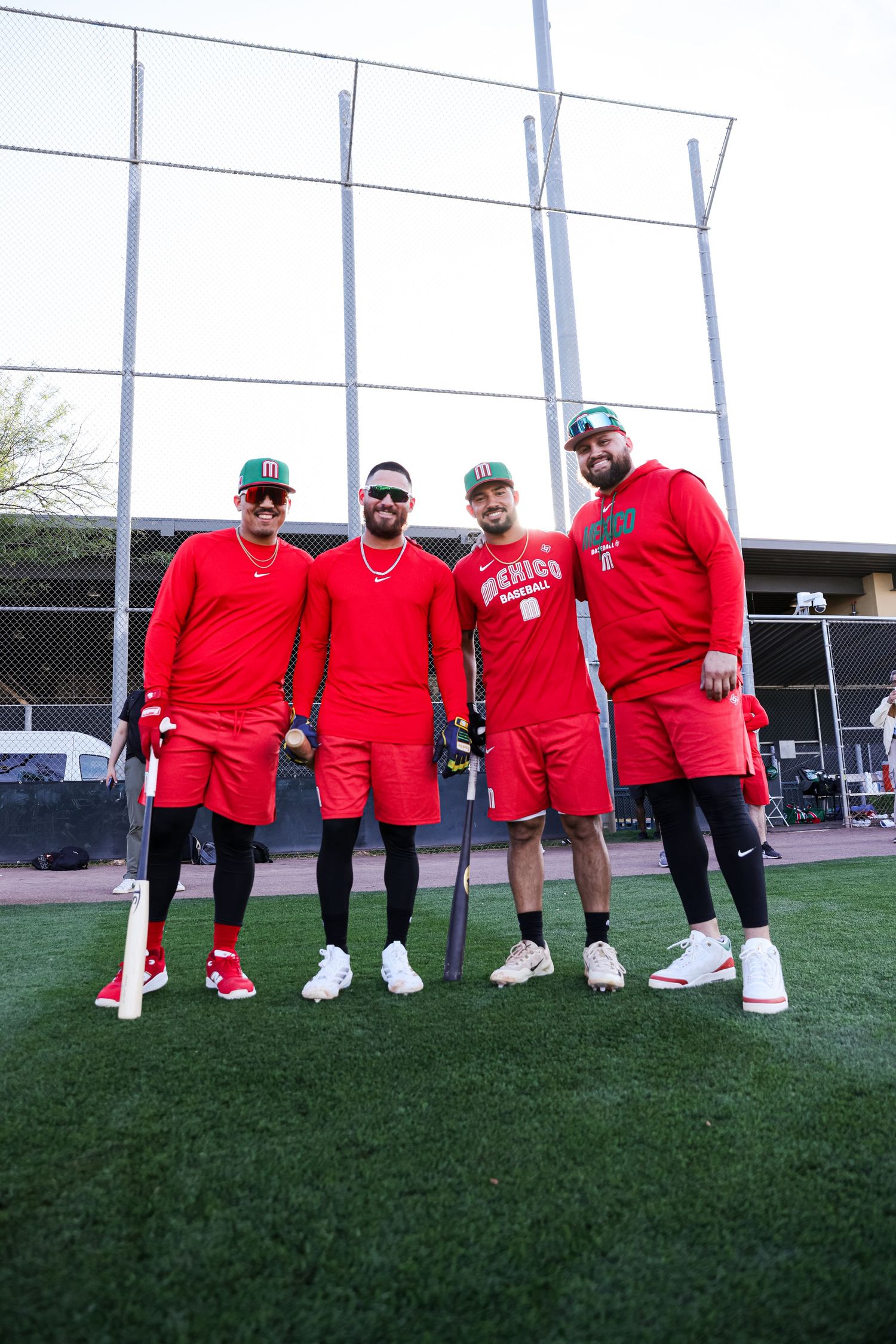 Four baseball players in red Mexico national team uniforms pose together on a practice field.