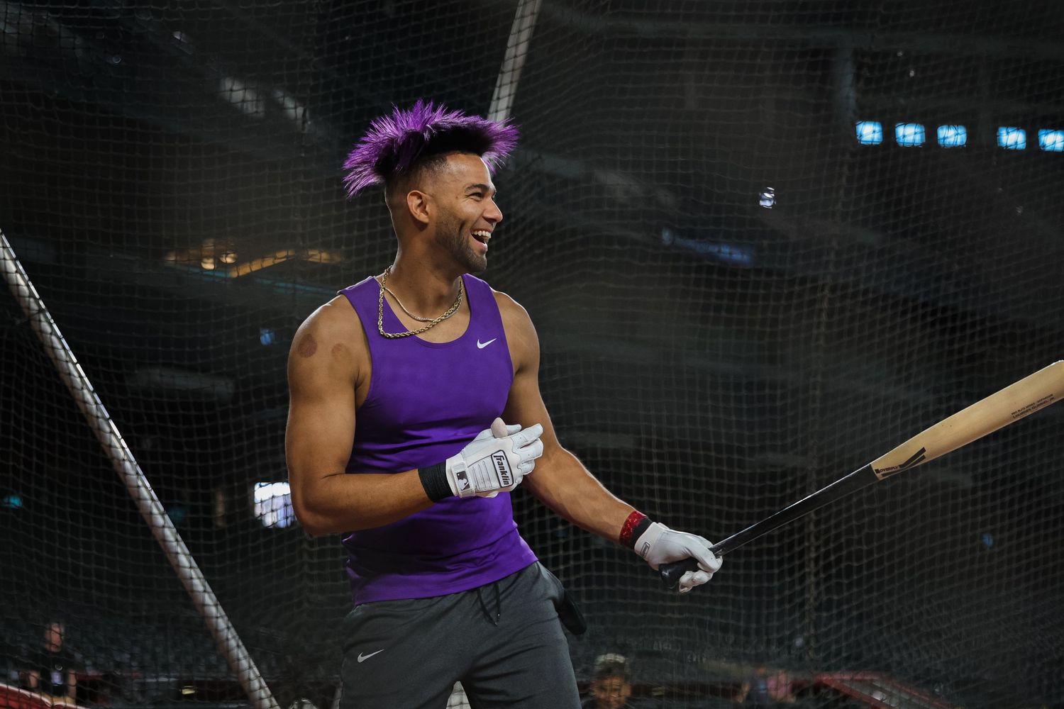 Baseball player with purple hair laughs during batting practice inside a stadium.