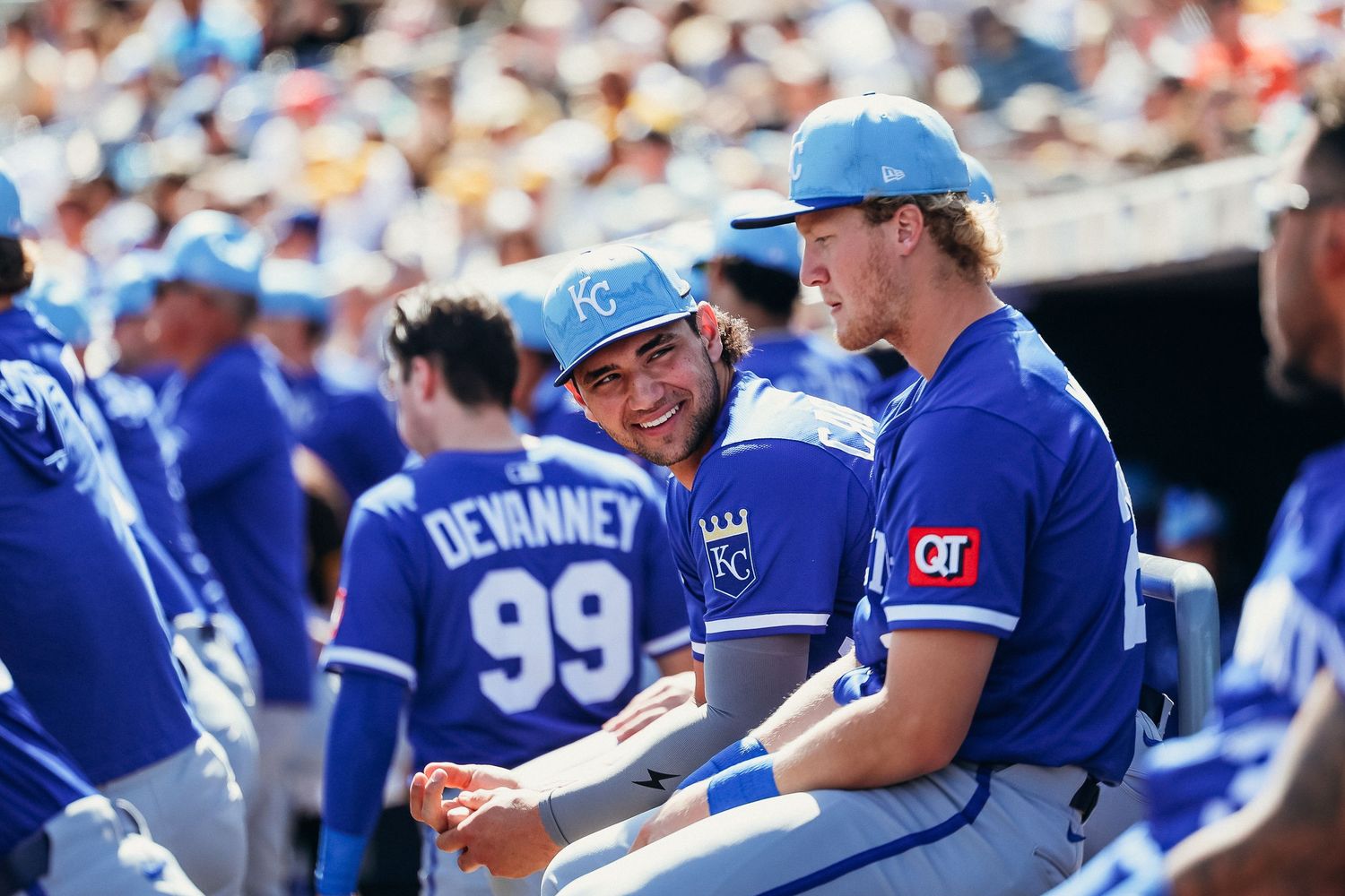 Kansas City Royals players smiling and chatting in the dugout during a sunny baseball game.