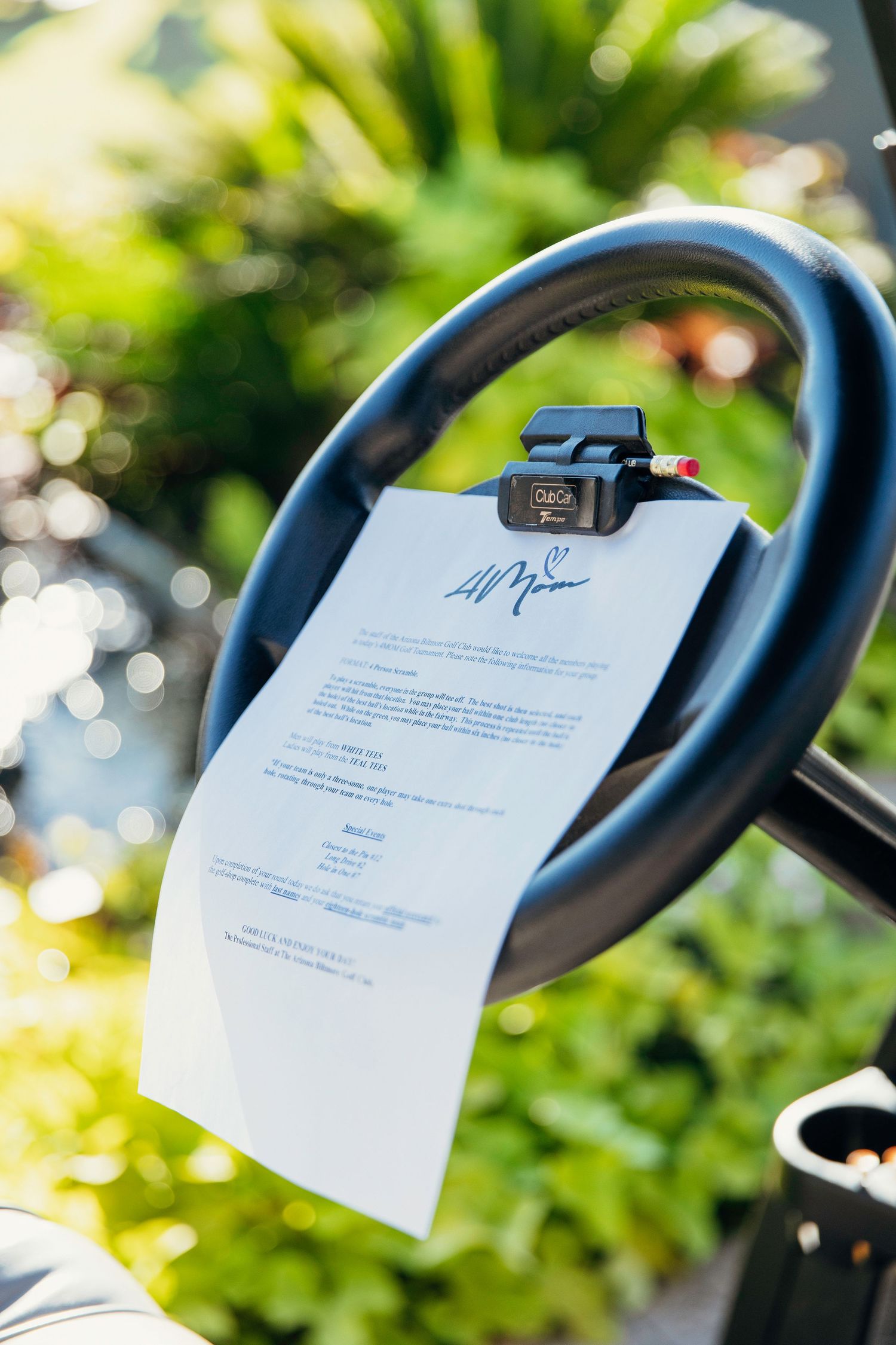 A signed document clipped to a golf cart steering wheel outdoors with lush green foliage in the background.