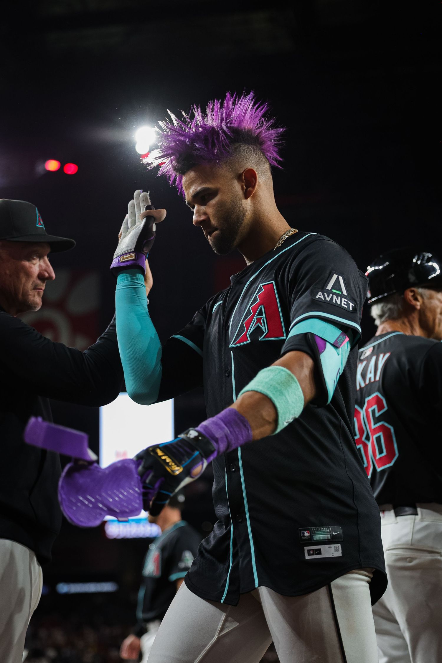 Baseball player with purple hair high-fiving teammates in dugout wearing Arizona Diamondbacks black jersey.