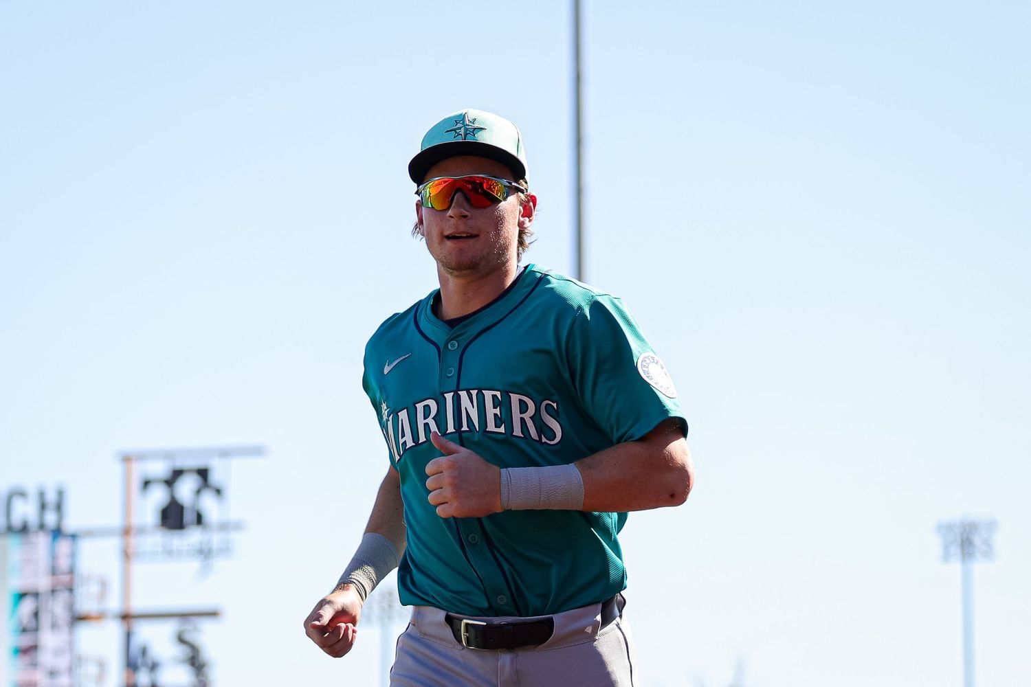 Seattle Mariners player jogging in teal uniform during spring training under bright sunlight.