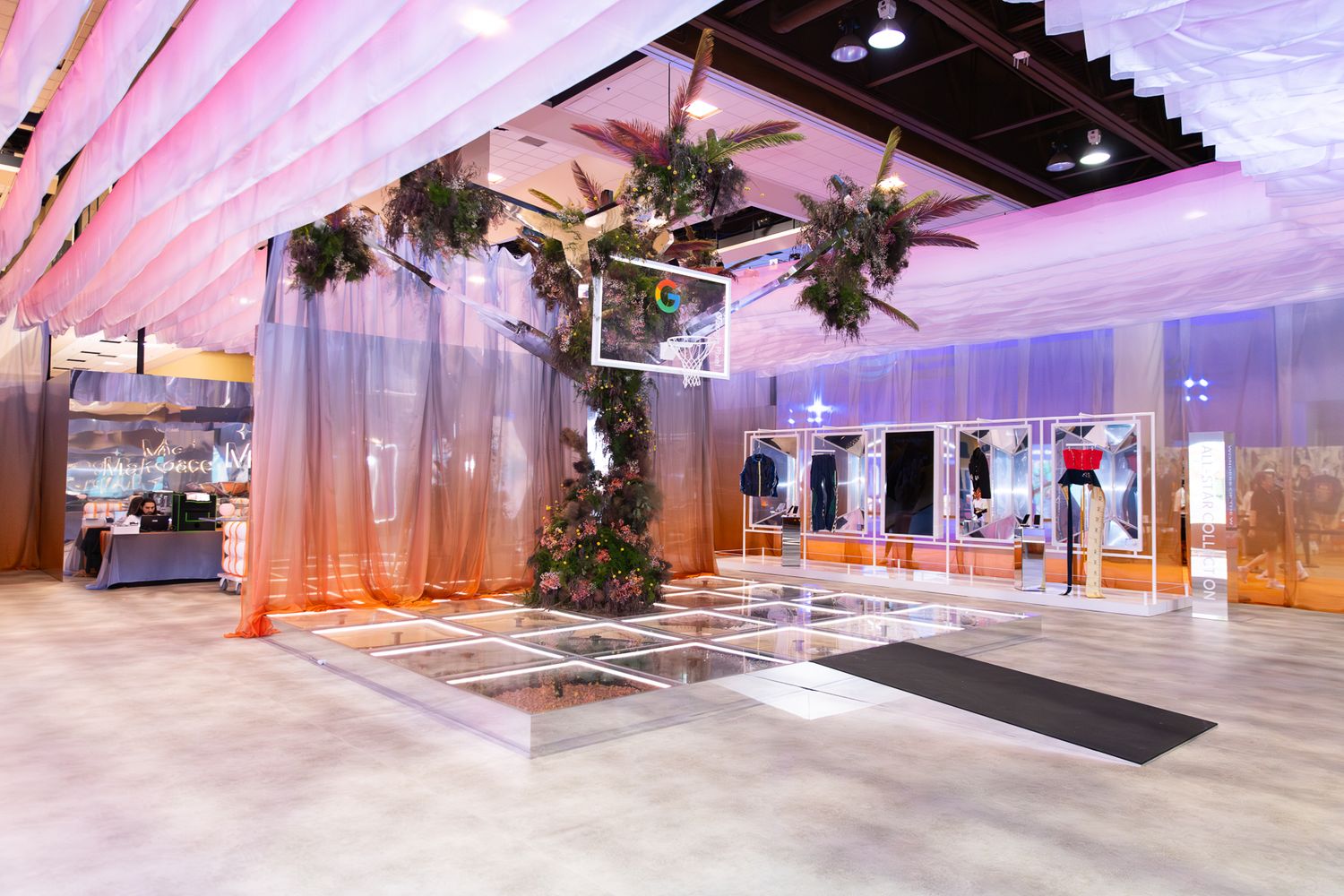 Modern event space entrance with tropical greenery installations, sheer curtains, and pink ambient lighting.