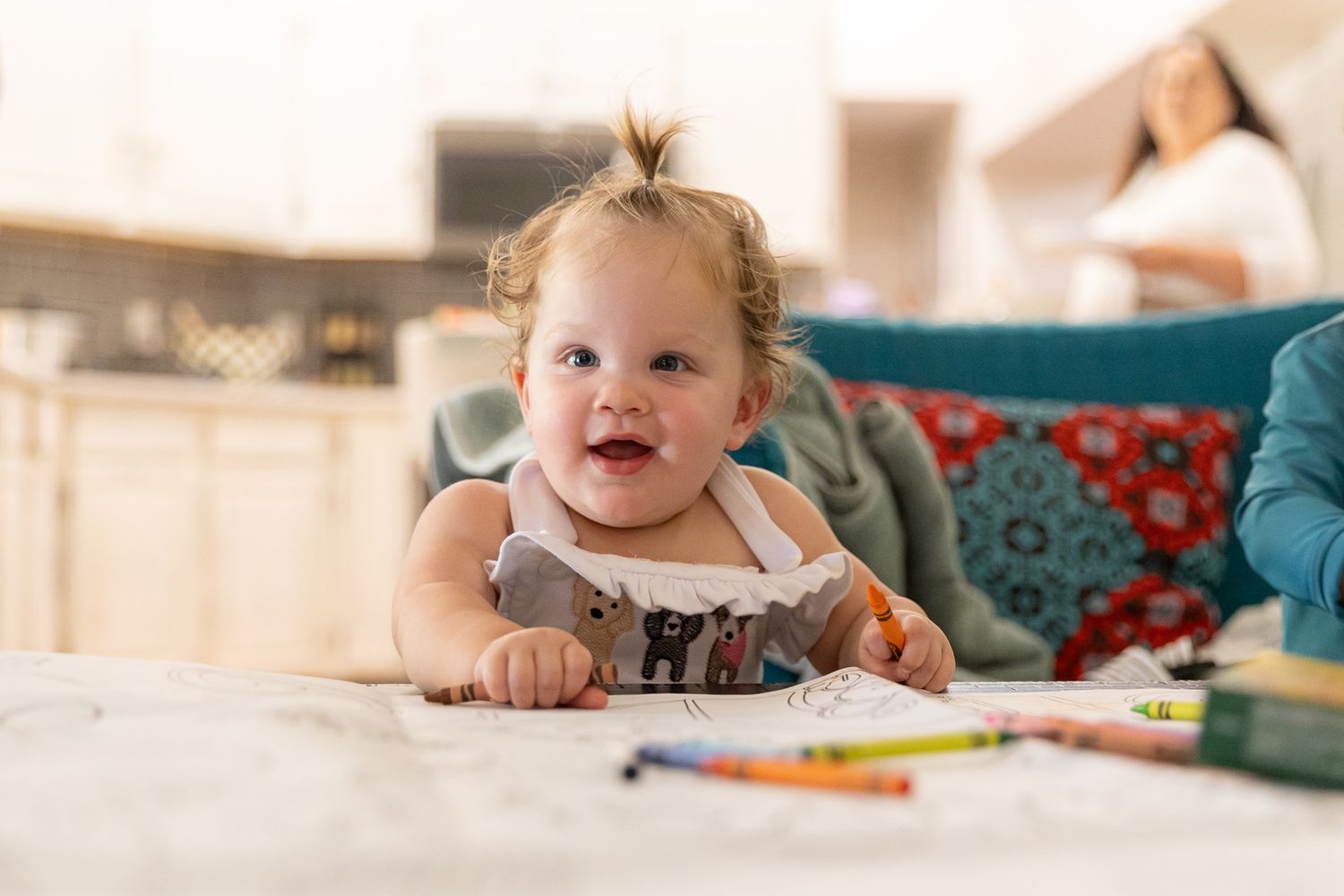 Happy baby lying on stomach on a bed smiling at the camera indoors.