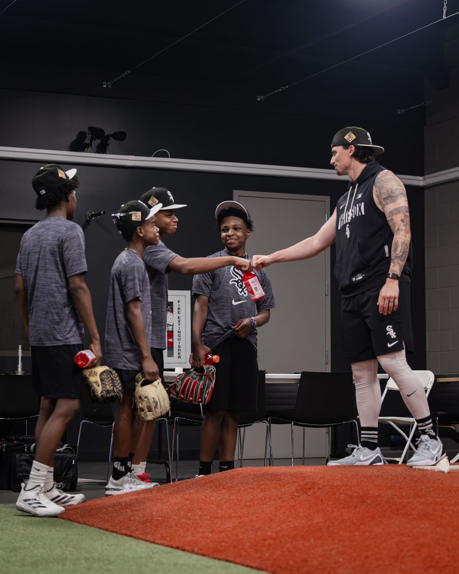 A tattooed baseball player shakes hands with young players wearing Chicago White Sox gear indoors.