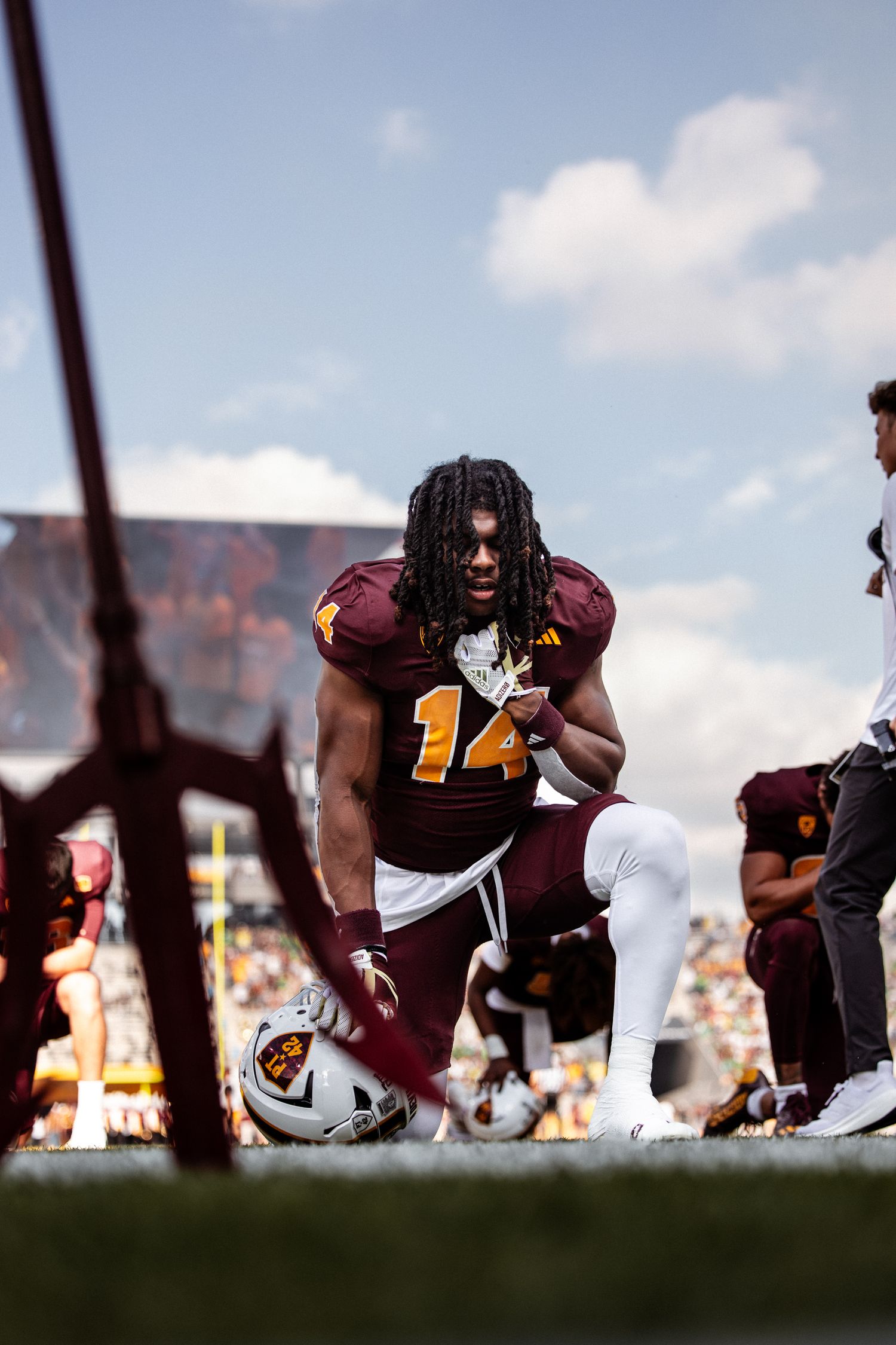 Arizona State Sun Devils football player number 14 kneels on field in maroon uniform during game day.