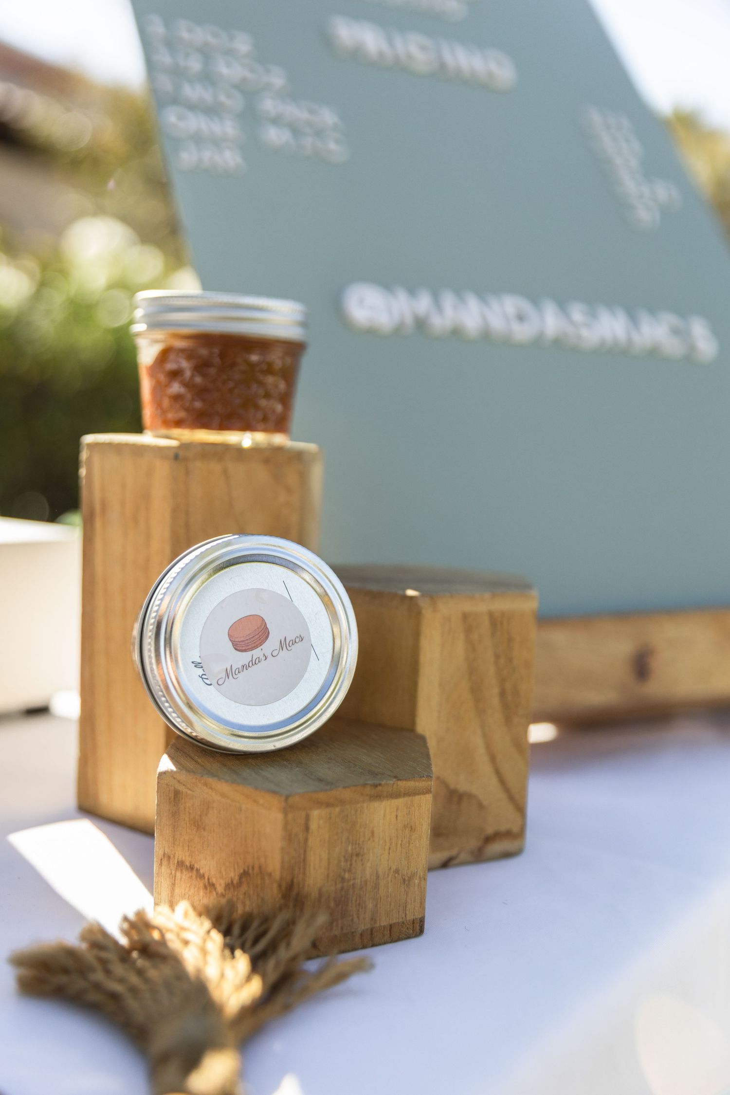 Mason jars of homemade jam displayed on wooden blocks at Manda's Macs vendor booth.