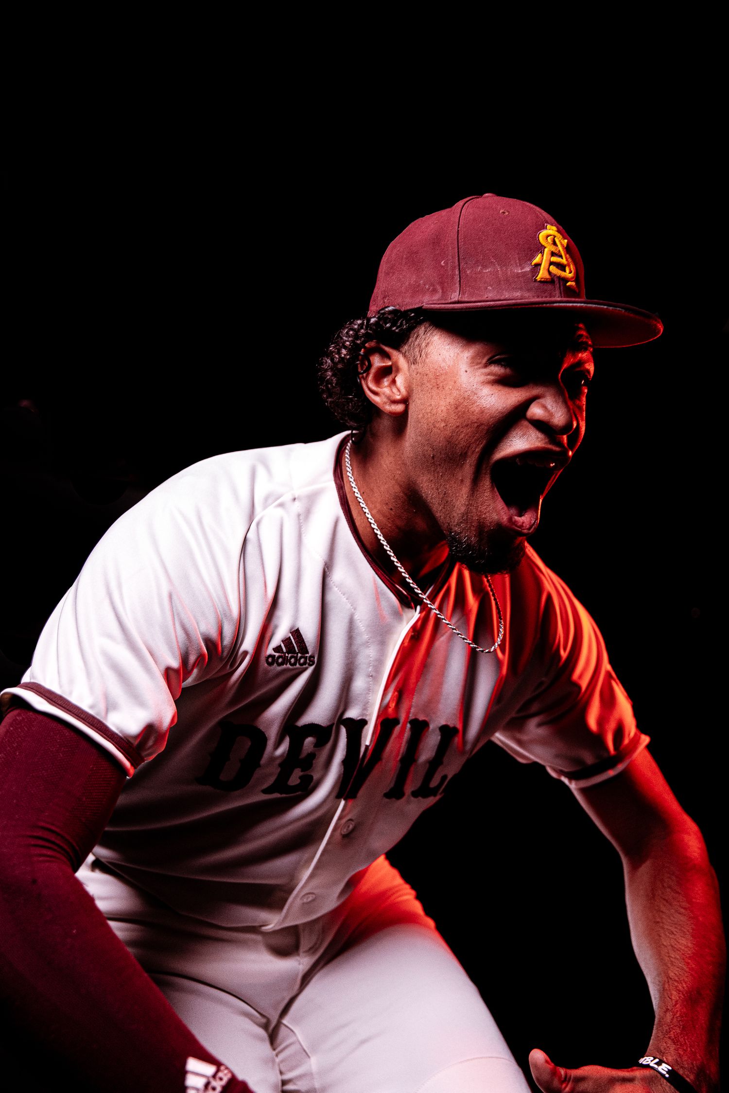 Arizona State Sun Devils baseball player celebrates intensely in maroon Adidas uniform under dramatic red lighting.