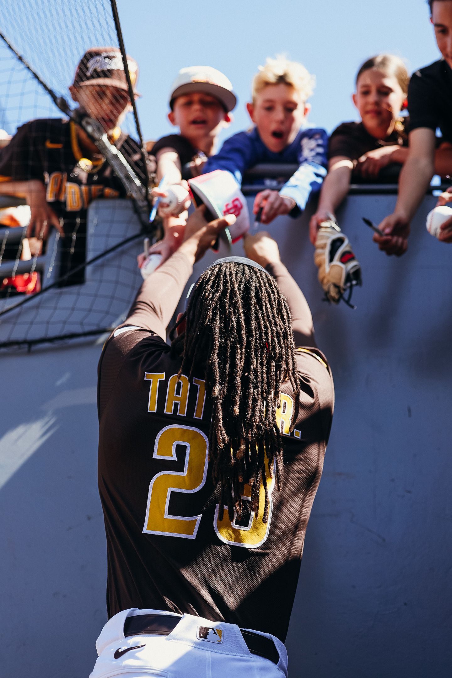 San Diego Padres player Tatis signing autographs for young fans leaning over stadium railing.