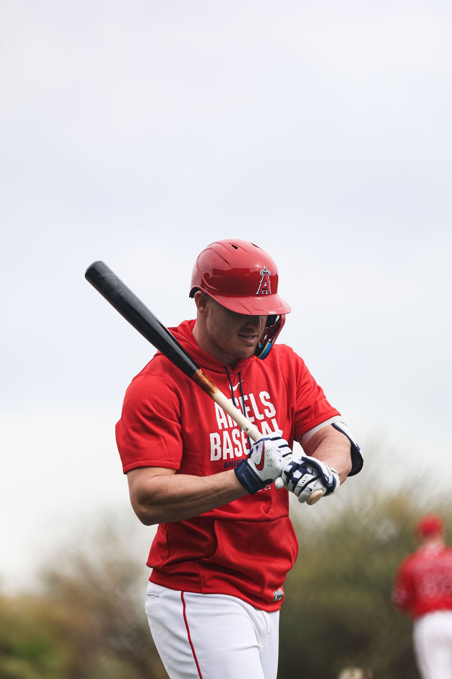 Angels Baseball player in red uniform holds bat during spring training practice session outdoors.