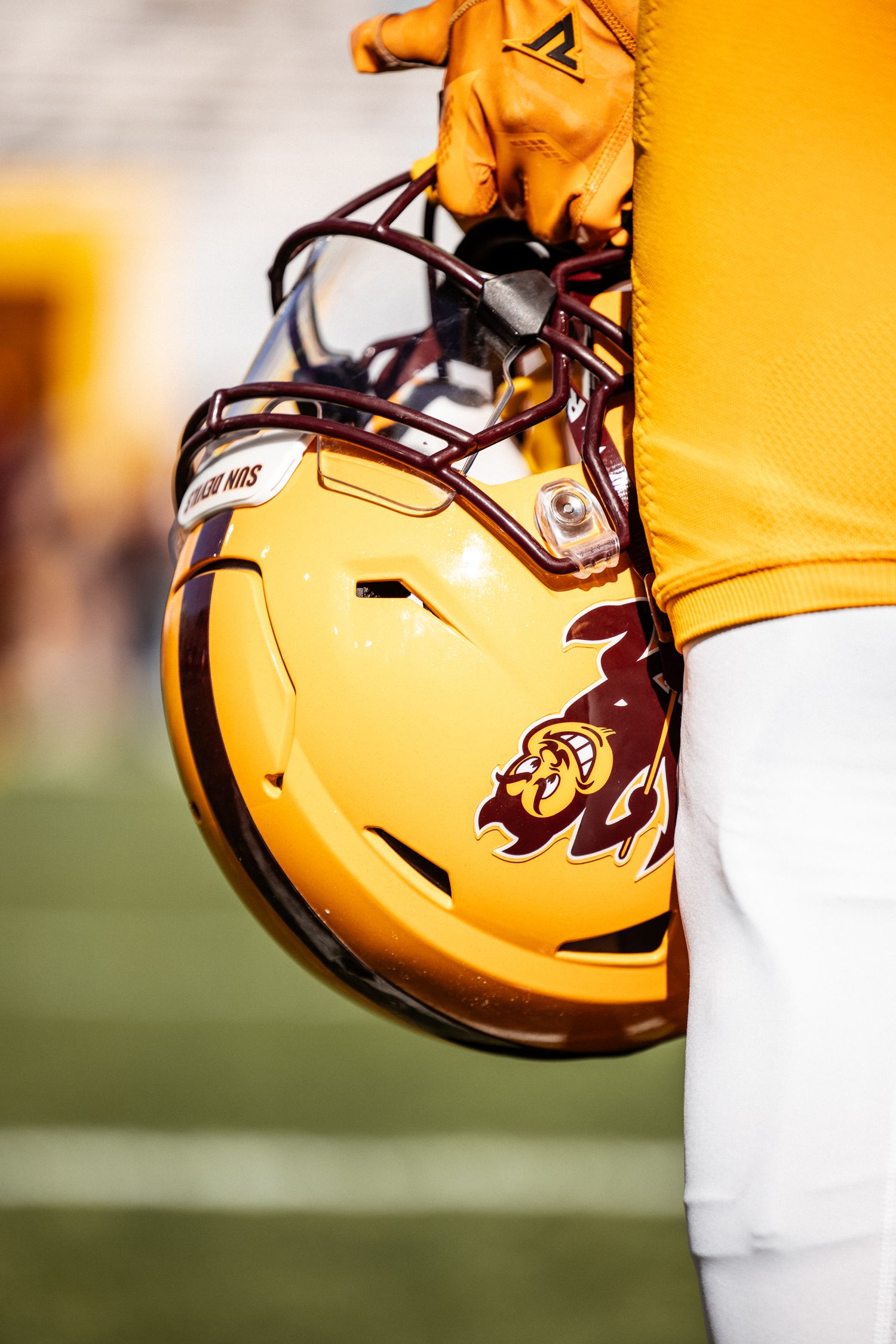 Arizona State Sun Devils football player holds gold helmet with Sparky logo in gold glove on sunny game day.