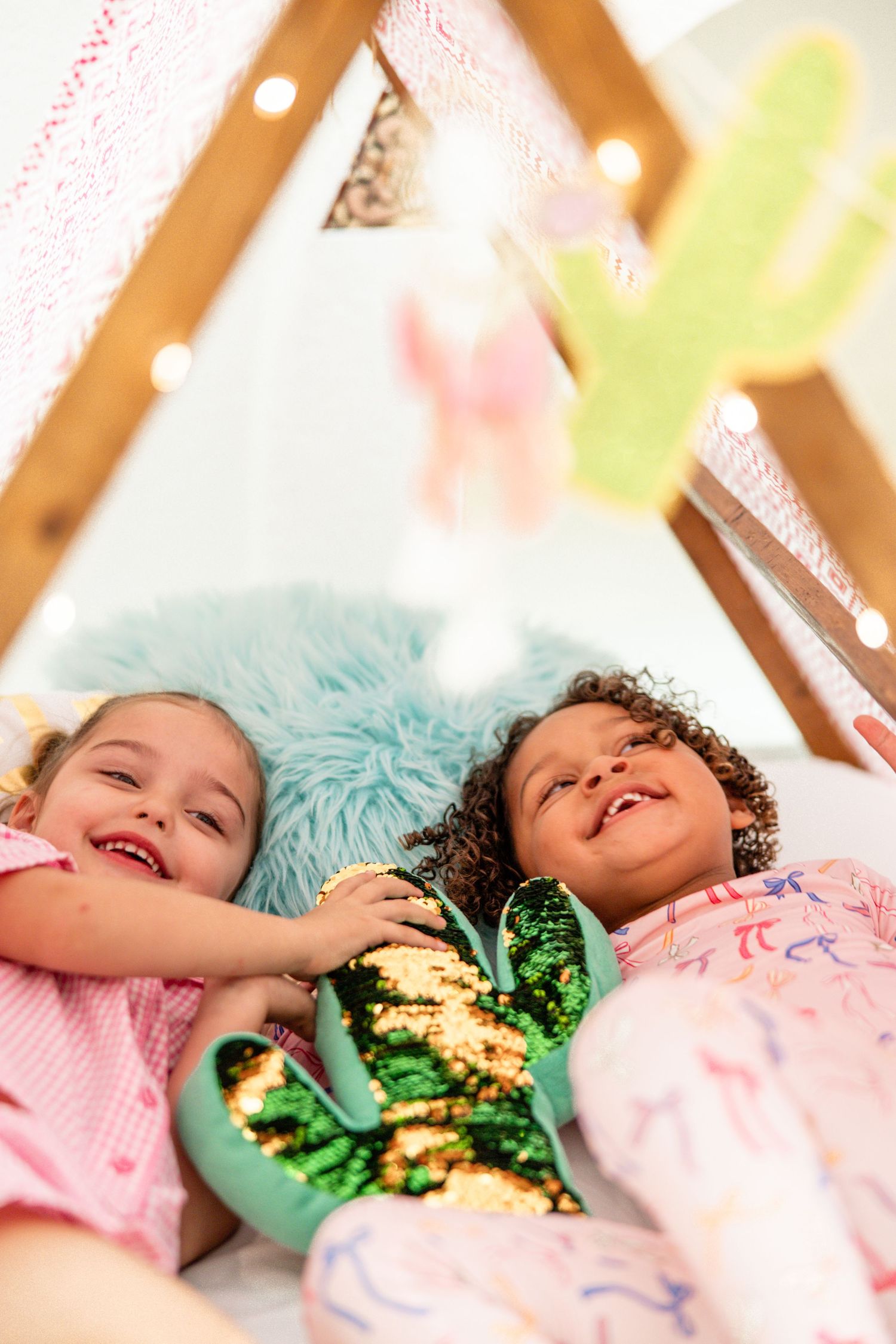 Two smiling girls lying inside a decorated teepee at a fun kids sleepover party.