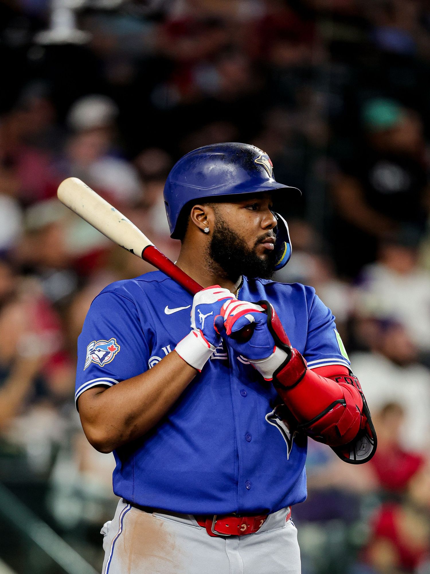 Toronto Blue Jays batter in blue uniform holds bat in ready stance wearing red batting gloves during MLB game.