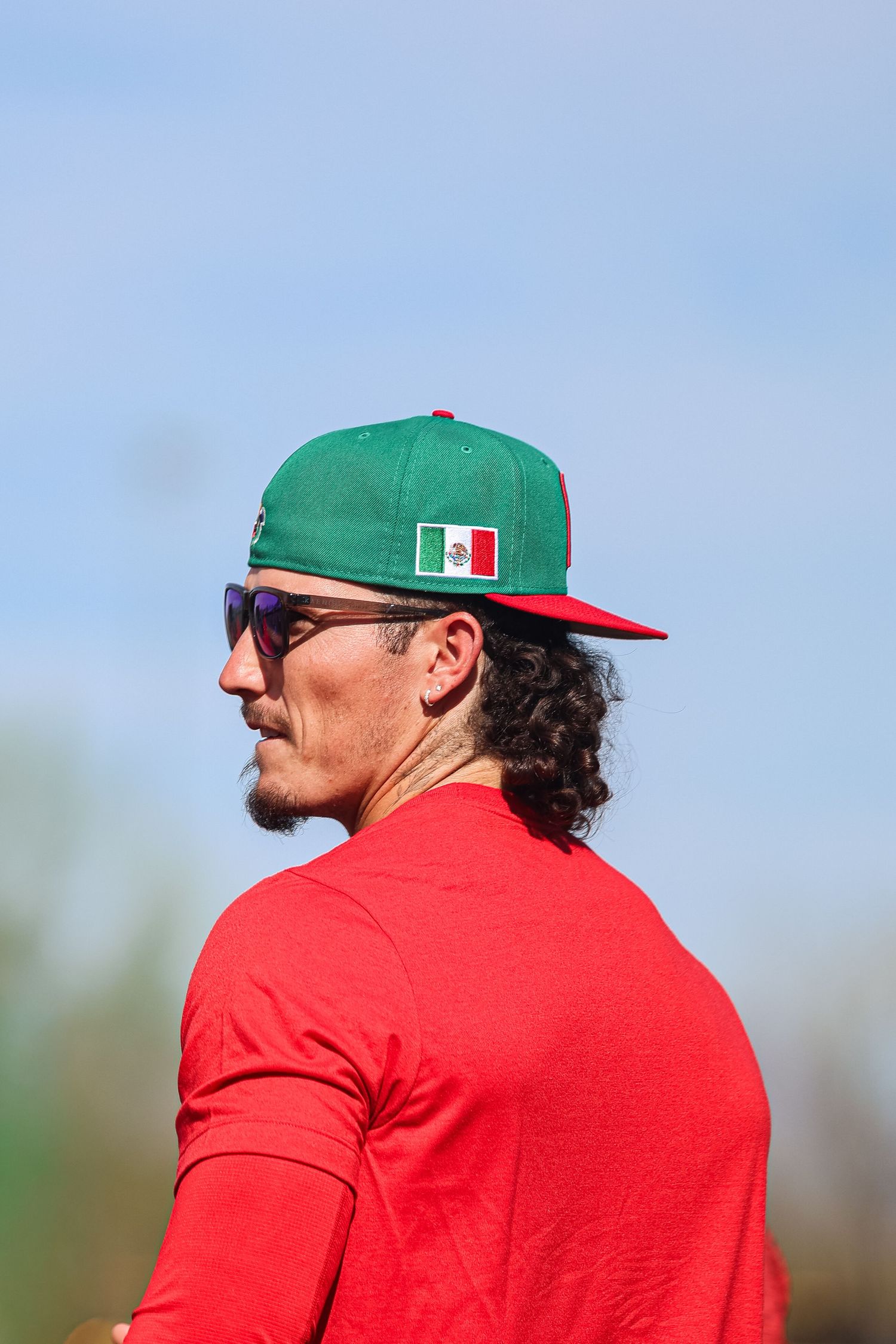 Baseball player in red Mexico uniform and green cap with Mexican flag patch looks sideways.