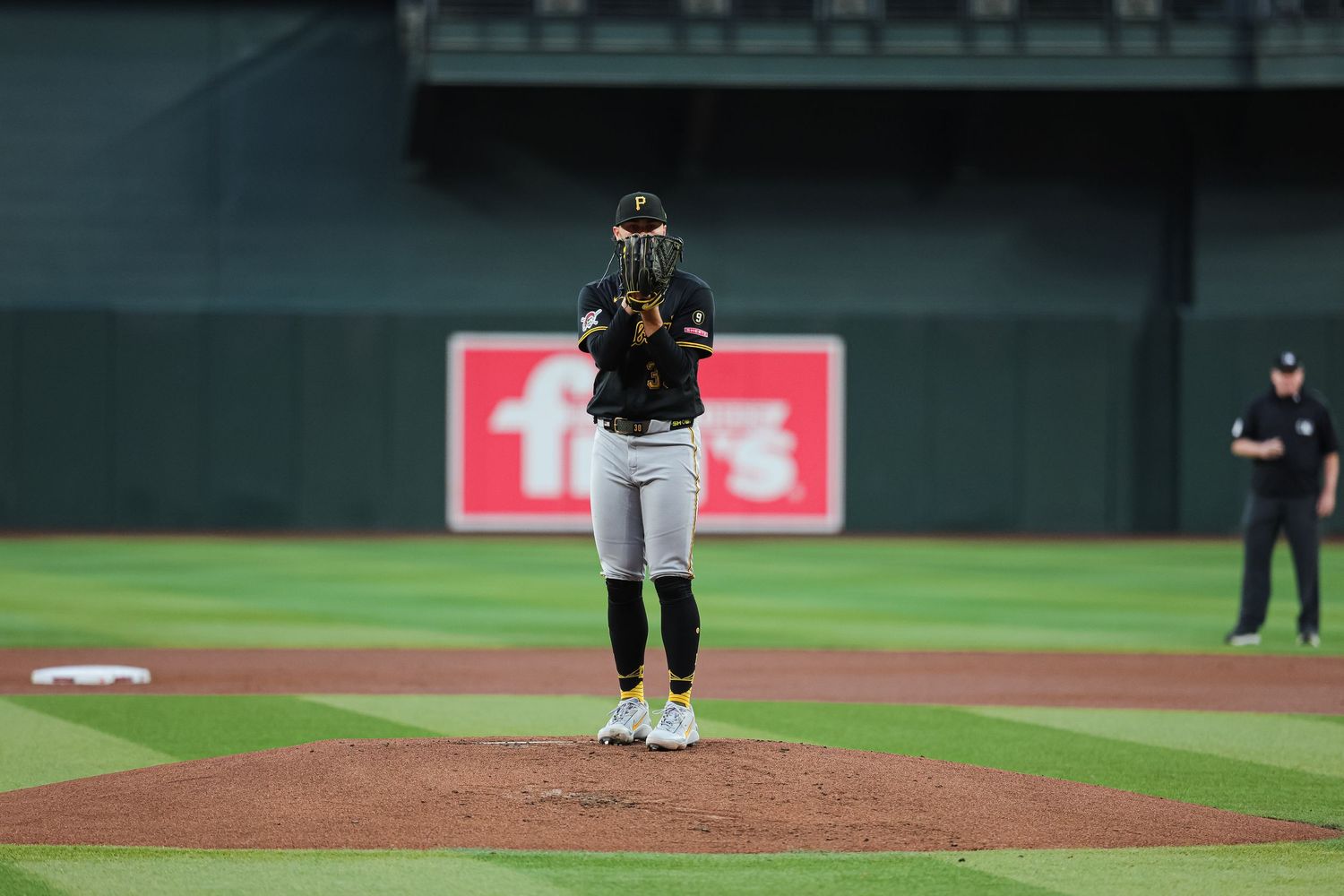 Baseball pitcher in black uniform stands on the mound in prayer position at an MLB stadium.