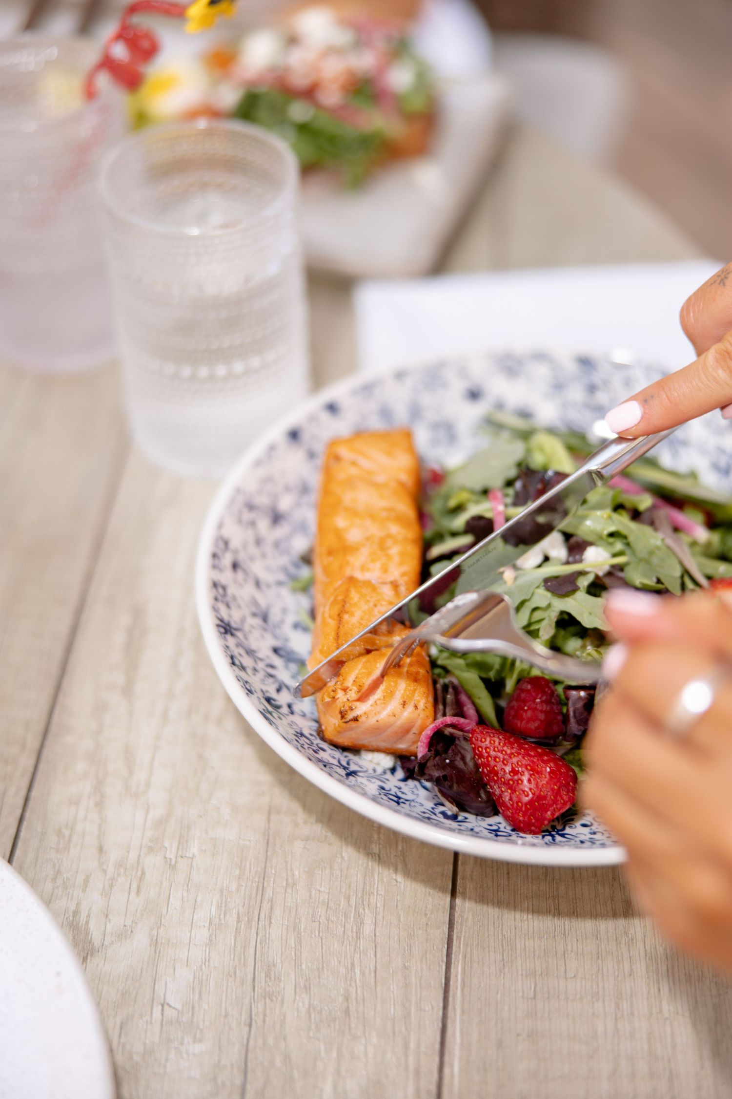 Person cutting grilled salmon on a fresh strawberry salad at a restaurant table.