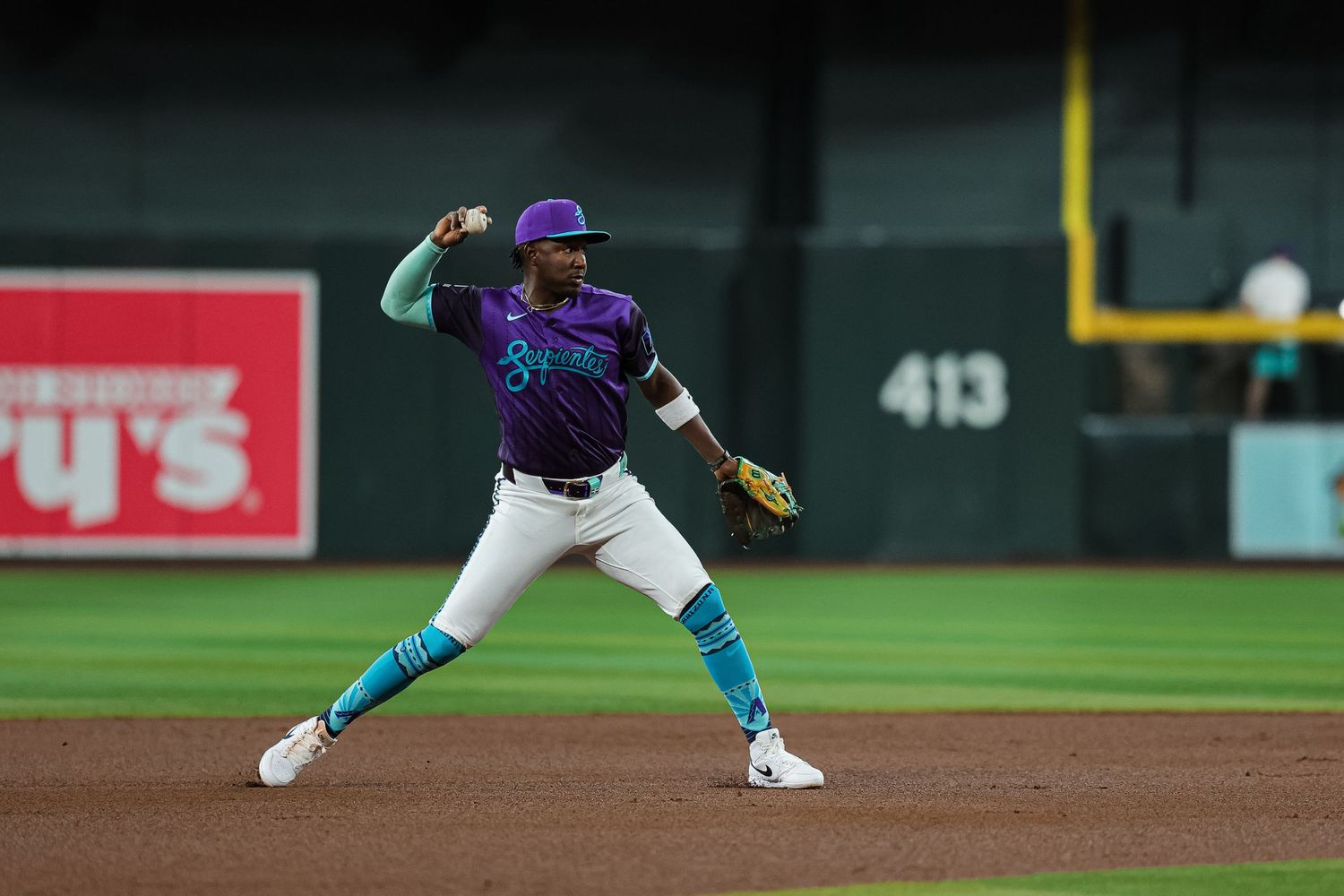 Arizona Diamondbacks infielder throws to first base in purple and teal uniform.