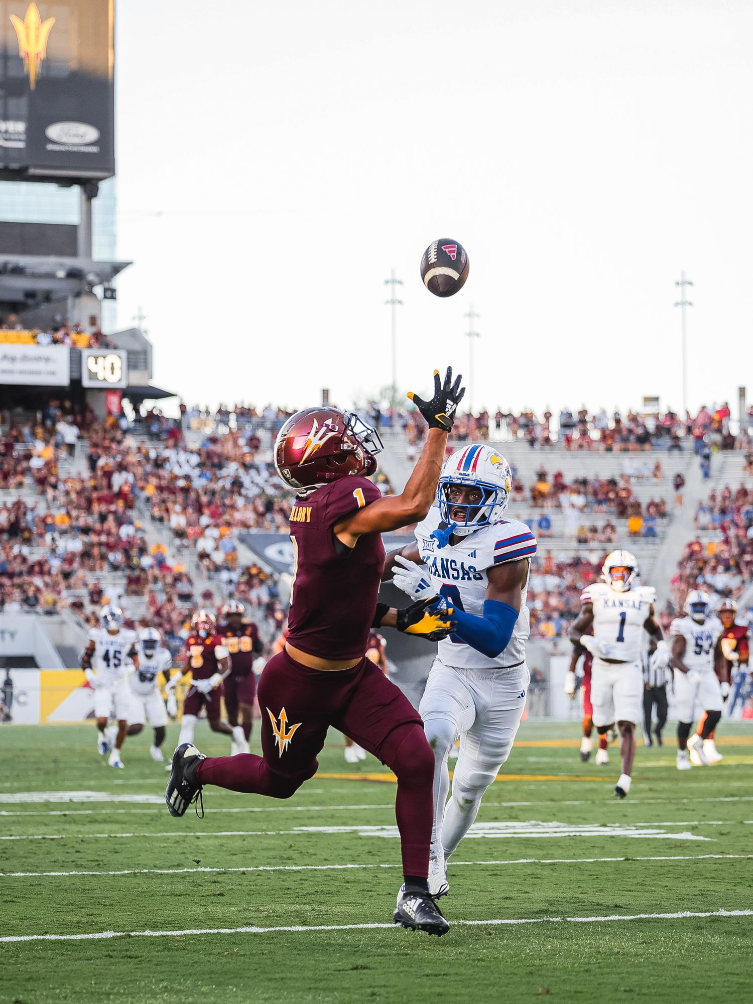Arizona State Sun Devils receiver attempts catch against Kansas defender in stadium.