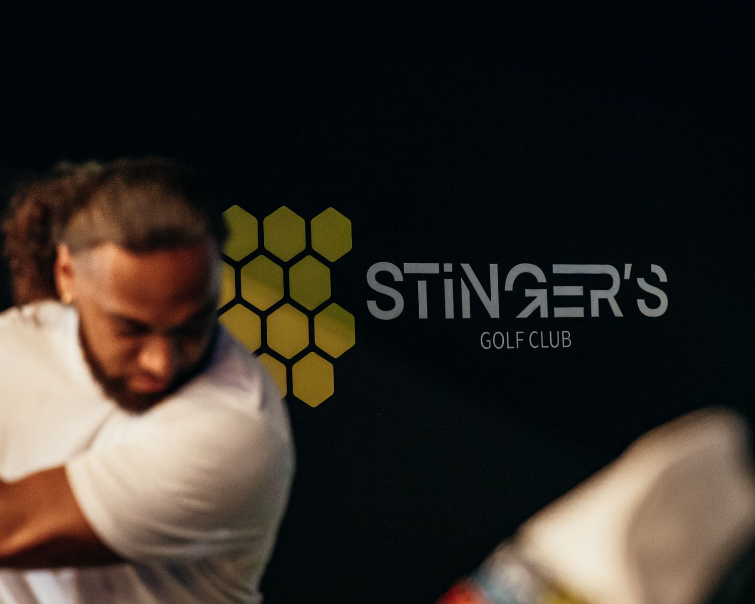 Golfer in white shirt swings club at Stinger's Golf Club, featuring a honeycomb logo design.