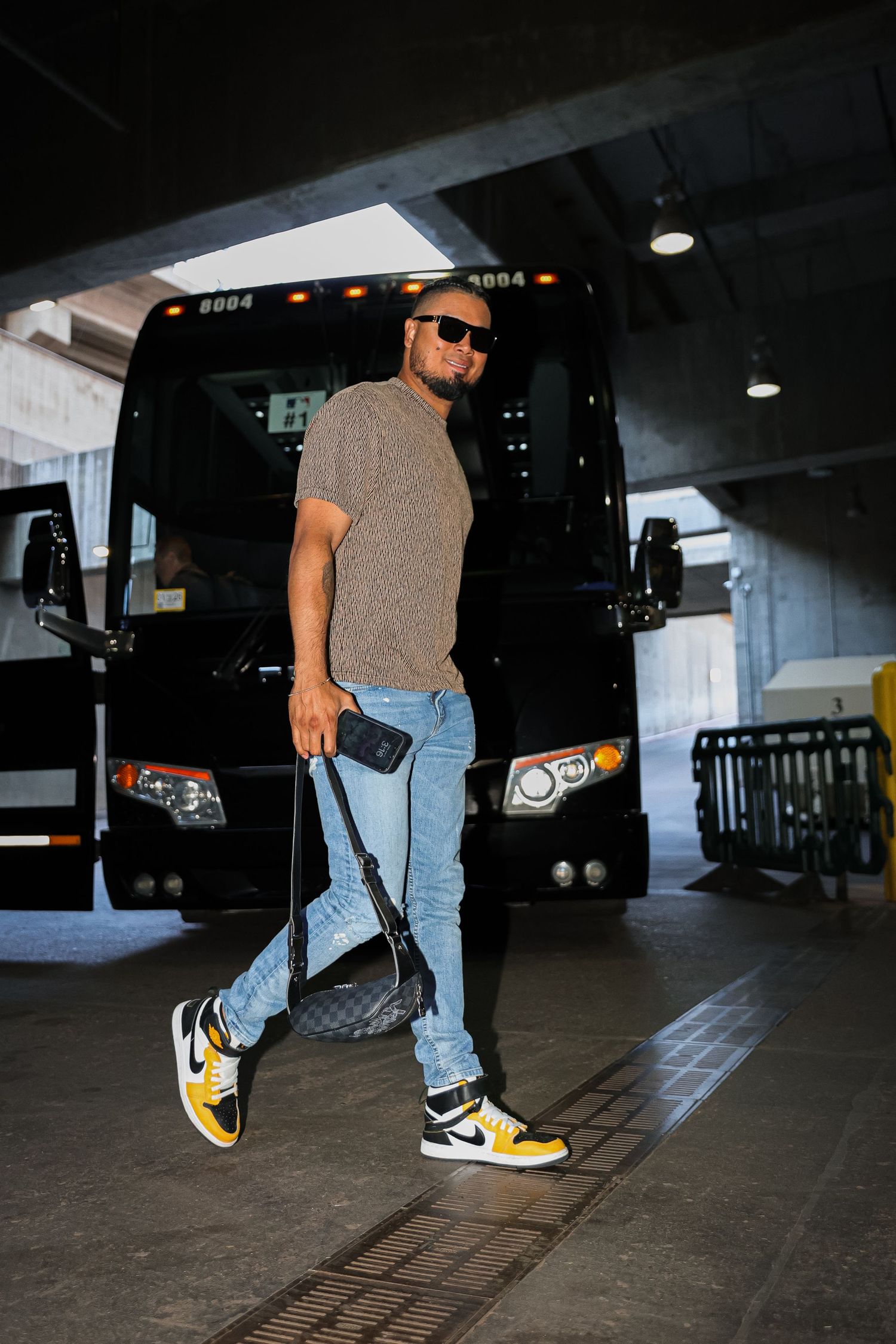 Male baseball player walking in casual outfit with yellow Nike sneakers near team bus.